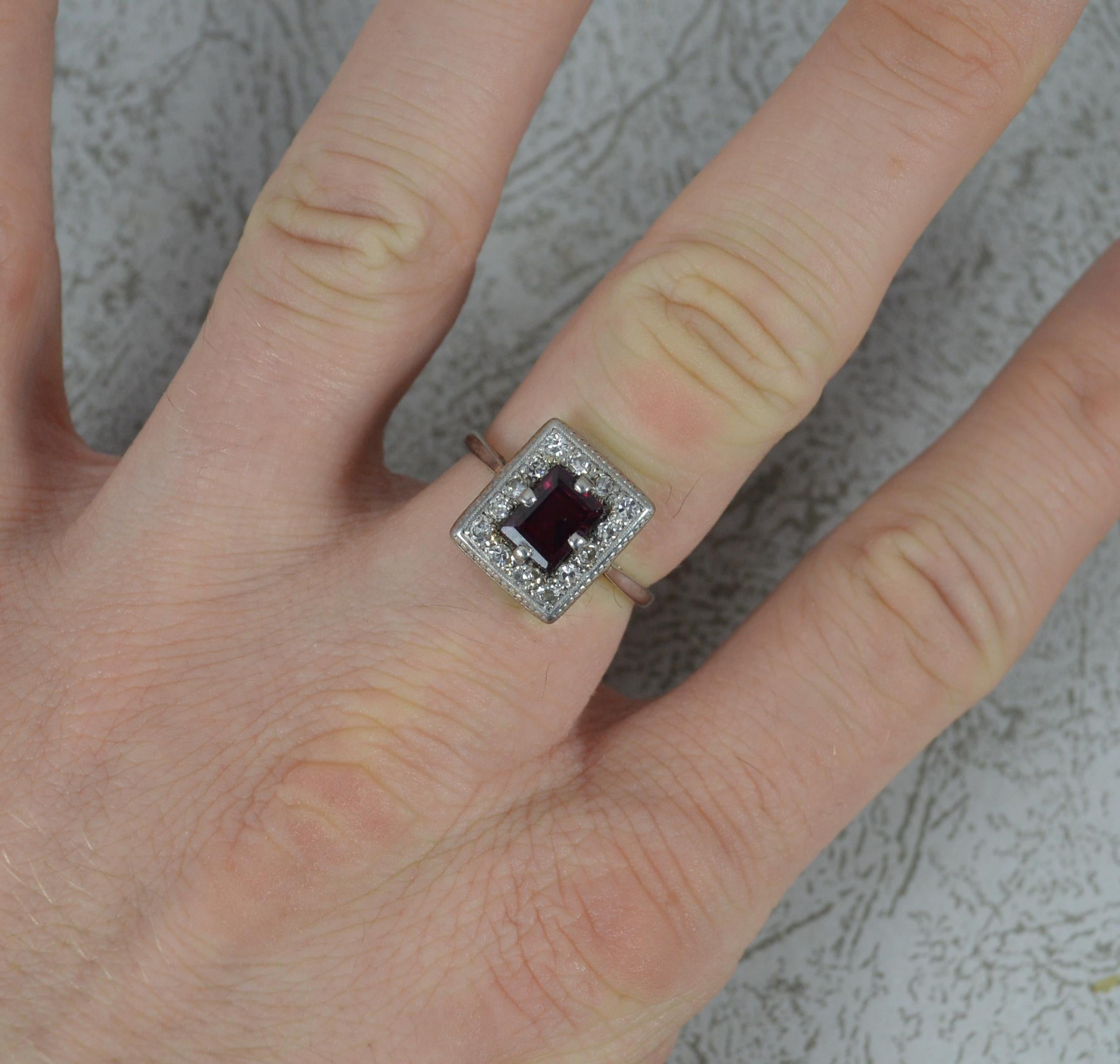 A superb Art Deco period panel cluster ring. c1930.
Solid 18 carat white gold example.
Designed with a rectangular cut garnet to centre with full round cut diamond border and engraved finish.
11mm x 12.5mm cluster head. Sitting snug to the