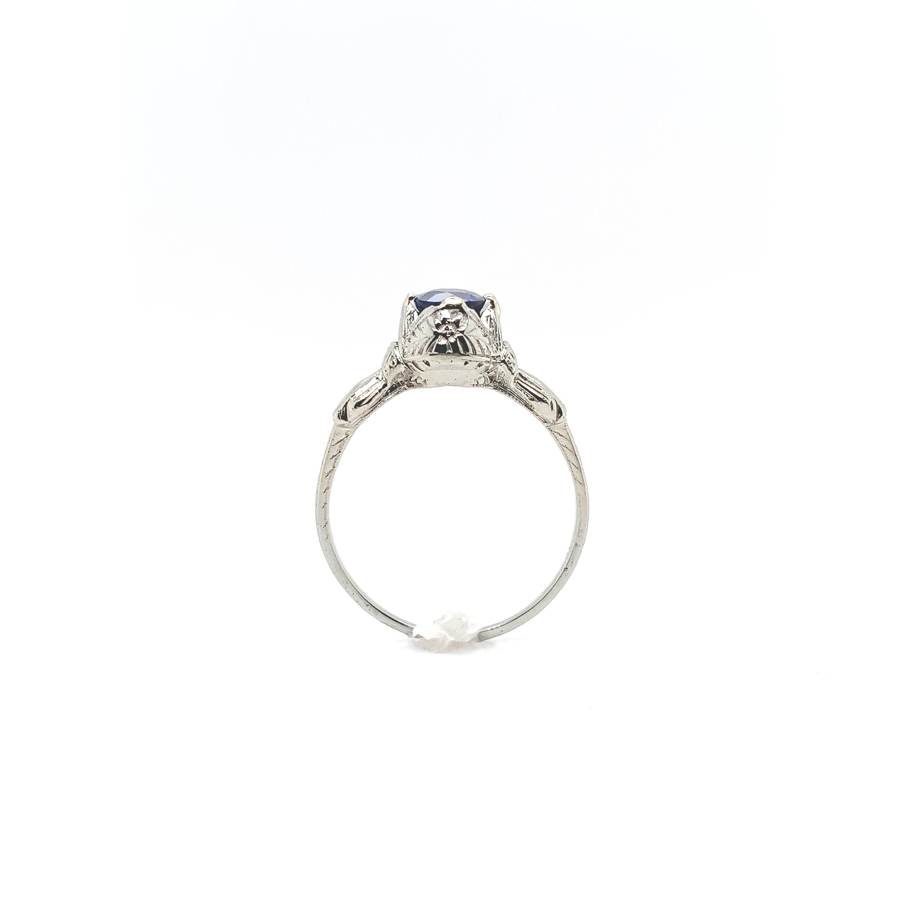 18K white gold ring featuring a genuine blue sapphire weighing .79ct. The round sapphire measures about 5.3mm. The setting is hand engraved on 3 sides. There is some wear to the underside where rings were worn beside this one. The prongs have all
