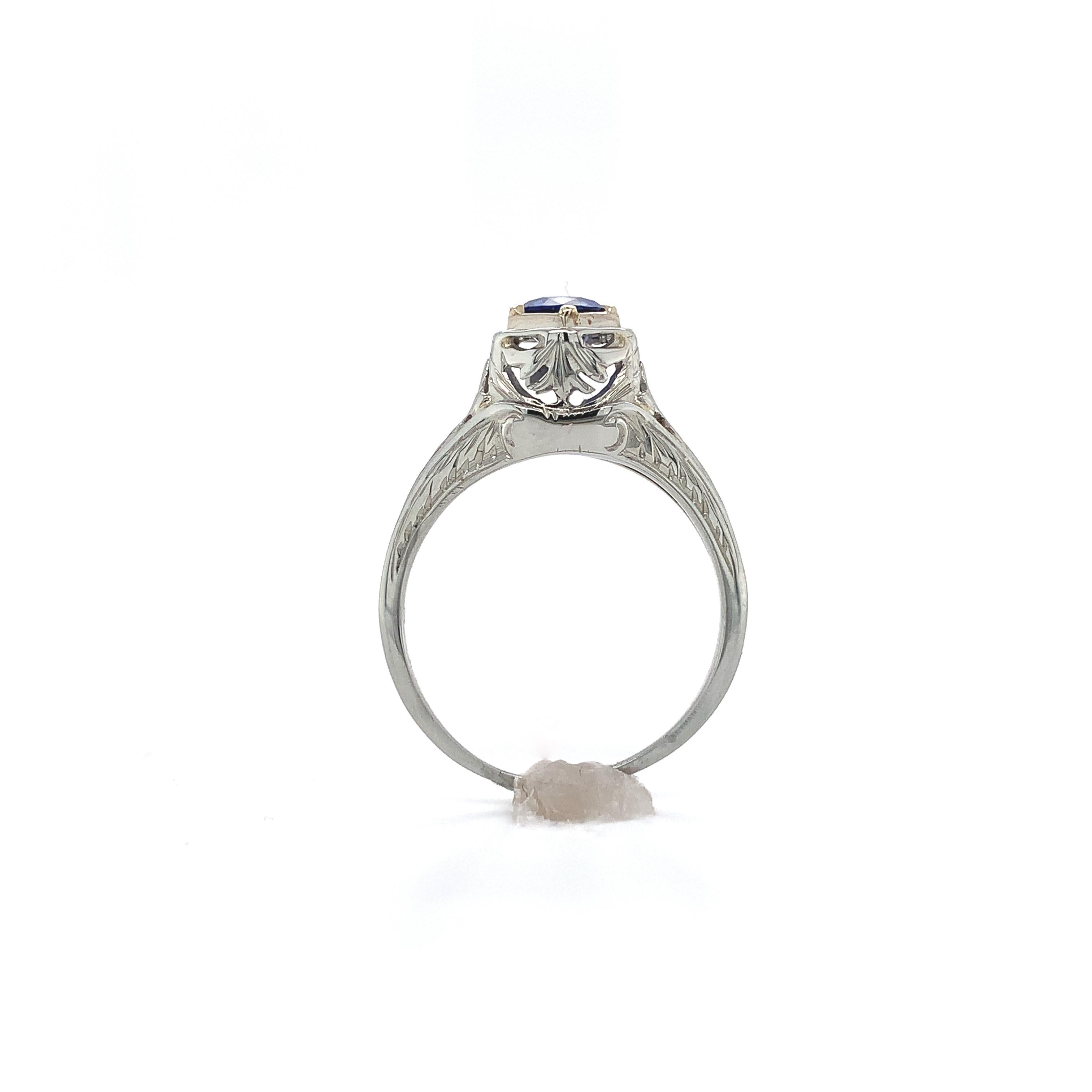 Art Deco 18K white gold filigree ring featuring a round genuine blue sapphire weighing .63cts. The sapphire has lighter cornflower blue with a little lavender color and measures about 5mm.  There is hand engraved detail and also a plain area where