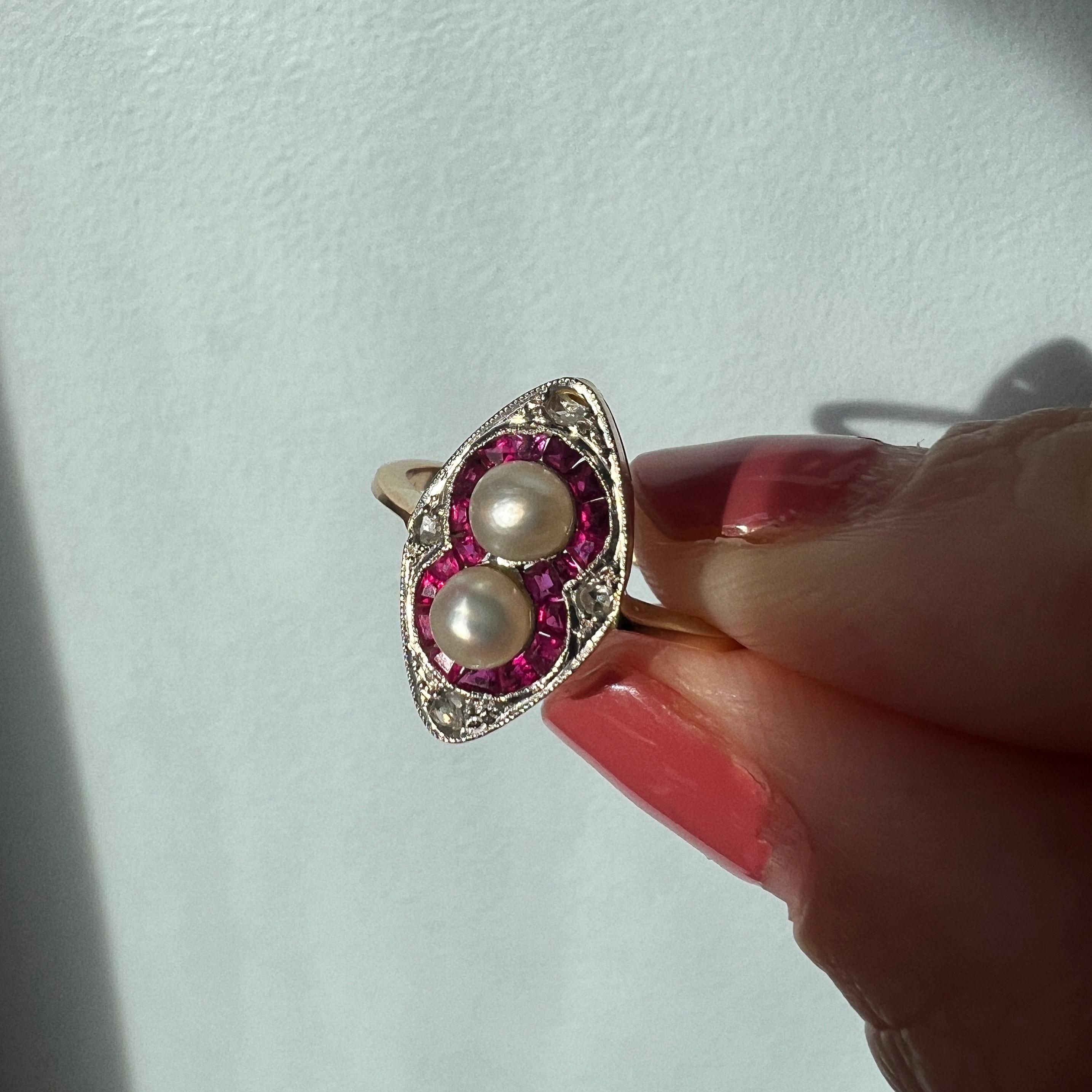 For sale a magnificence 18K gold ring from the Art Deco era. This stunning ring features a pair of lustrous white pearls, delicately nestled within a meticulously crafted setting of calibrated vivid red rubies.

The central motif, an elegantly