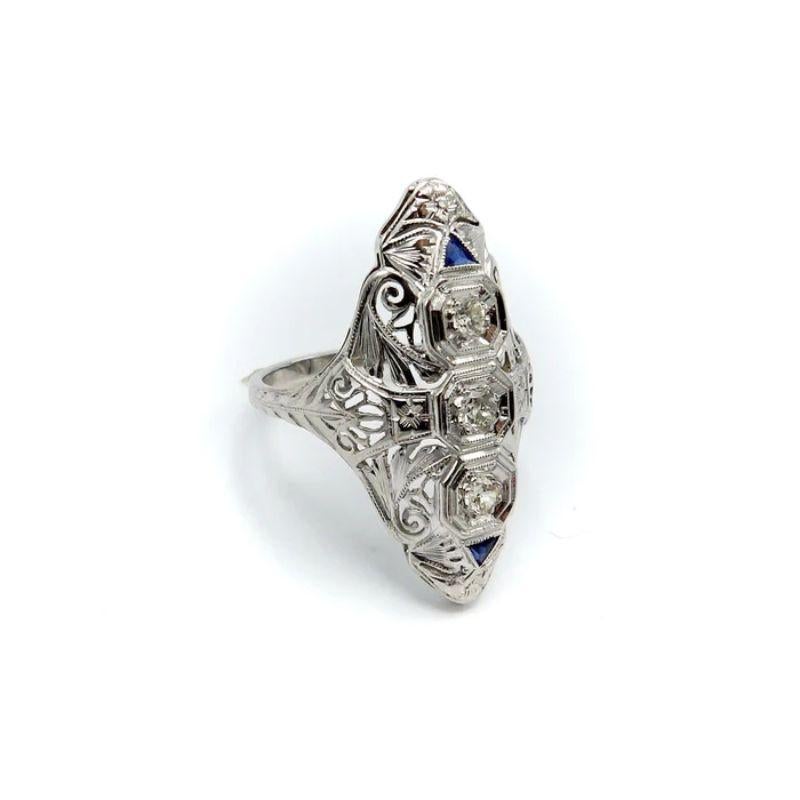 This is a stunning Art Deco navette-shaped 18 karat white gold, diamond and sapphire ring. The ring has some excellent filigree work that merges organic abstract shaped with sharp angular lines. 

The center diamond measures 3.35 mm, and the