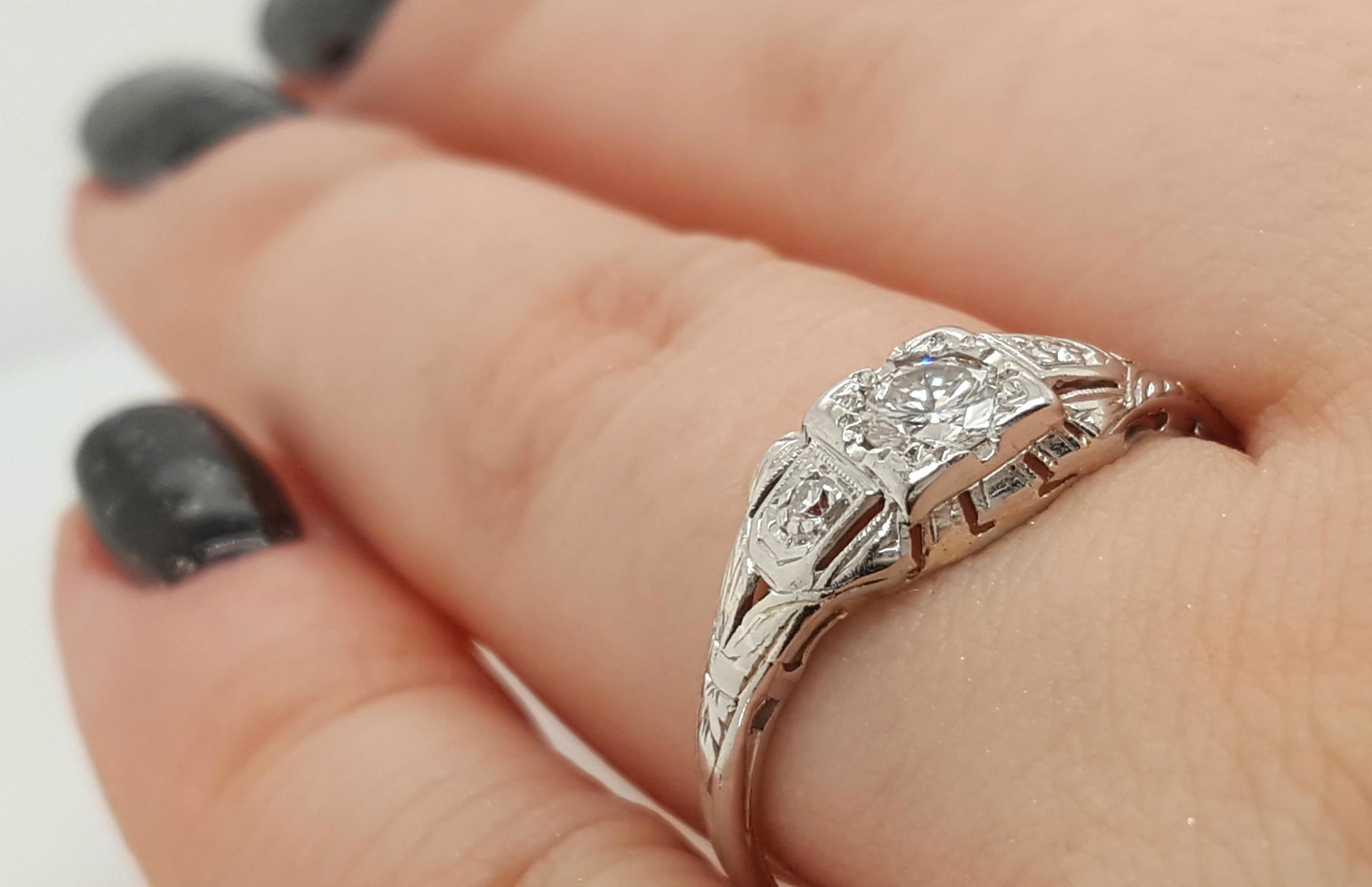 This gorgeous 18 karat white gold Art Deco vintage engagement ring features a modified round brilliant cut diamond set in four fishtail prongs, weighing approximately 0.26 carats, VS2 - SI1 in clarity I - J in color. Two single cut diamonds are