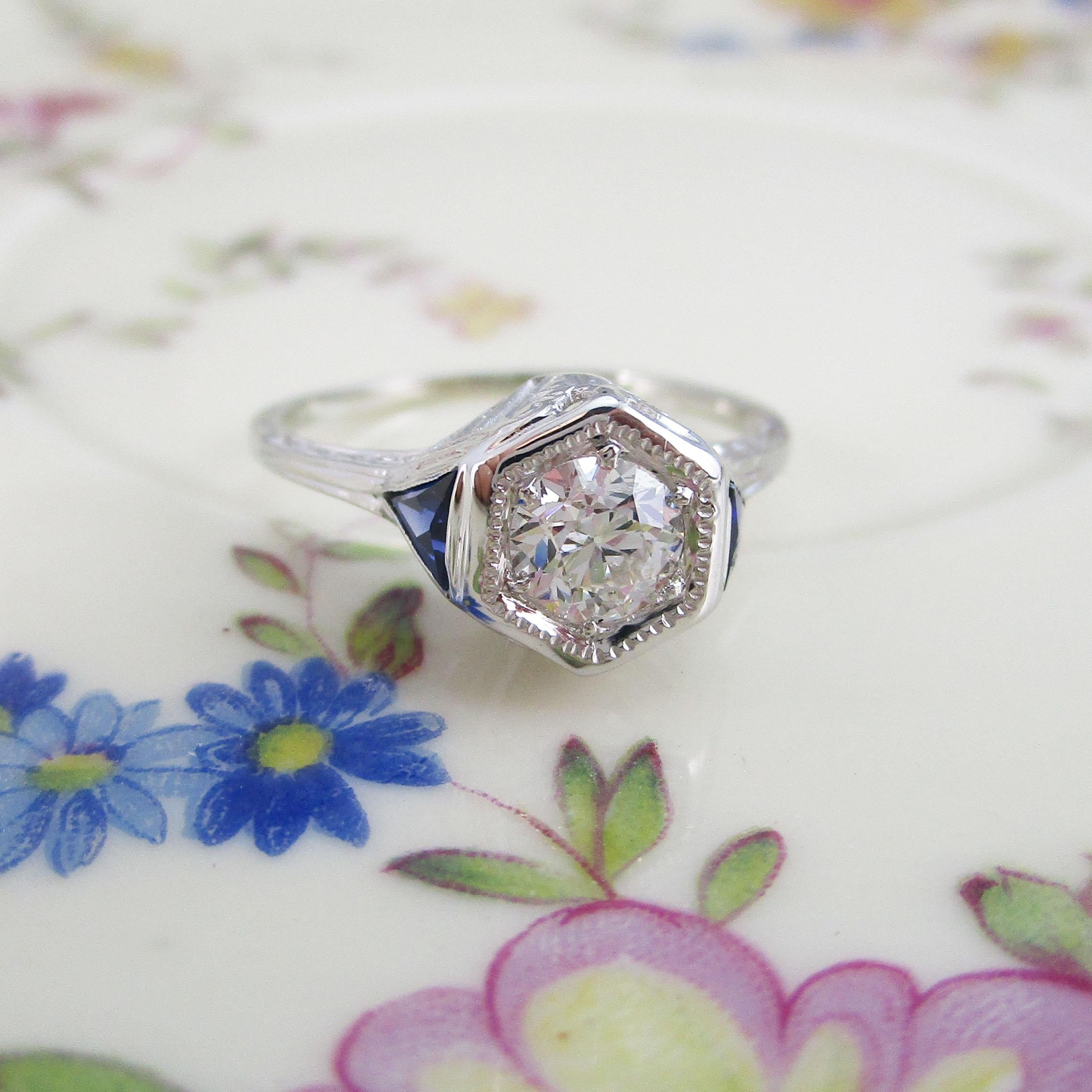 This is a breathtaking original Art Deco engagement ring in 18k white gold with a beautiful old mine cut diamond center flanked by two beautiful blue sapphires!! This ring has a few of the classic hallmarks of Art Deco - an elegant raised head, a