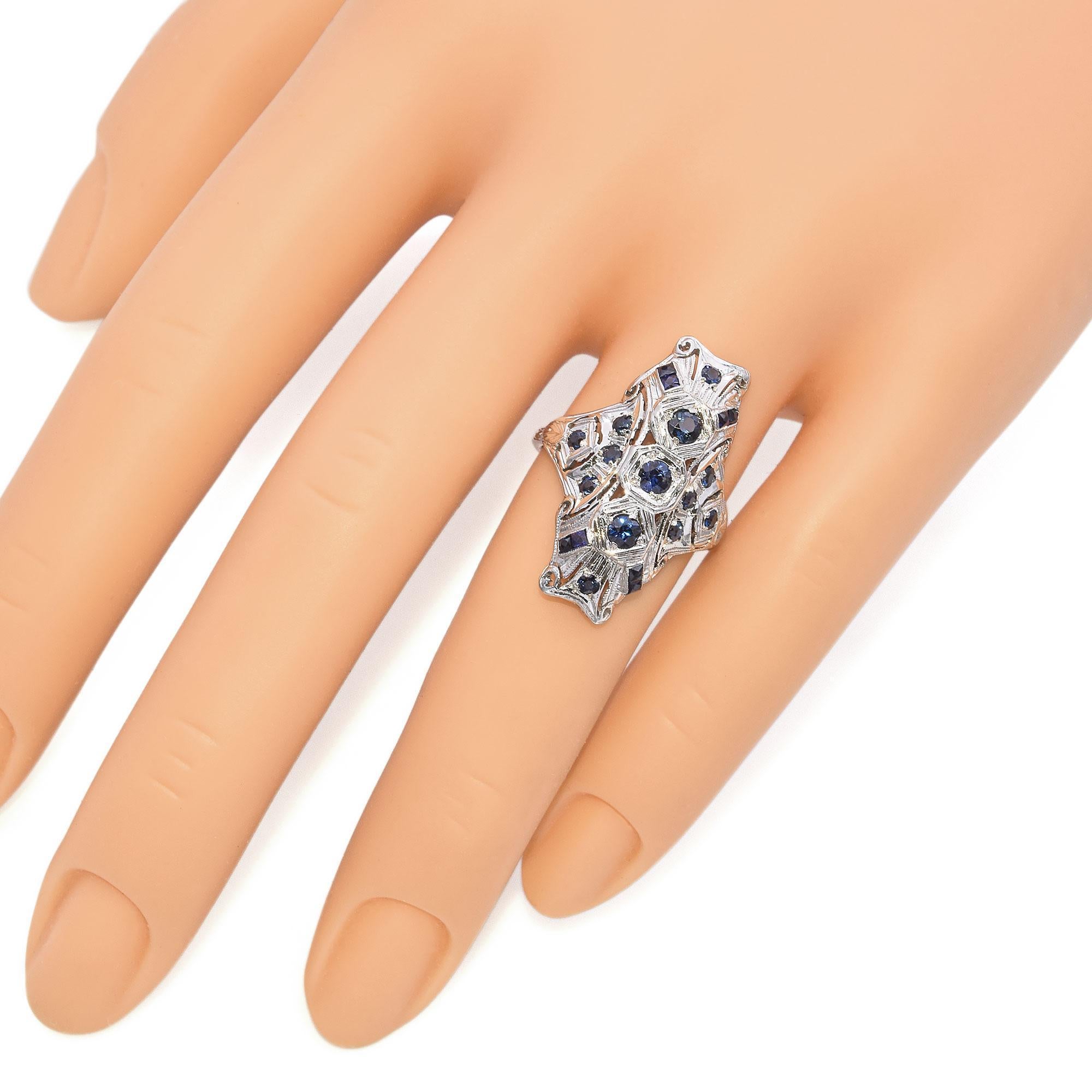 Une bague en saphir et or blanc, d'une beauté saisissante. Il présente plusieurs saphirs ronds et carrés d'un bleu profond. Les saphirs de laboratoire et les saphirs naturels sont sertis de façon complexe dans un motif ajouré orné, créant un motif