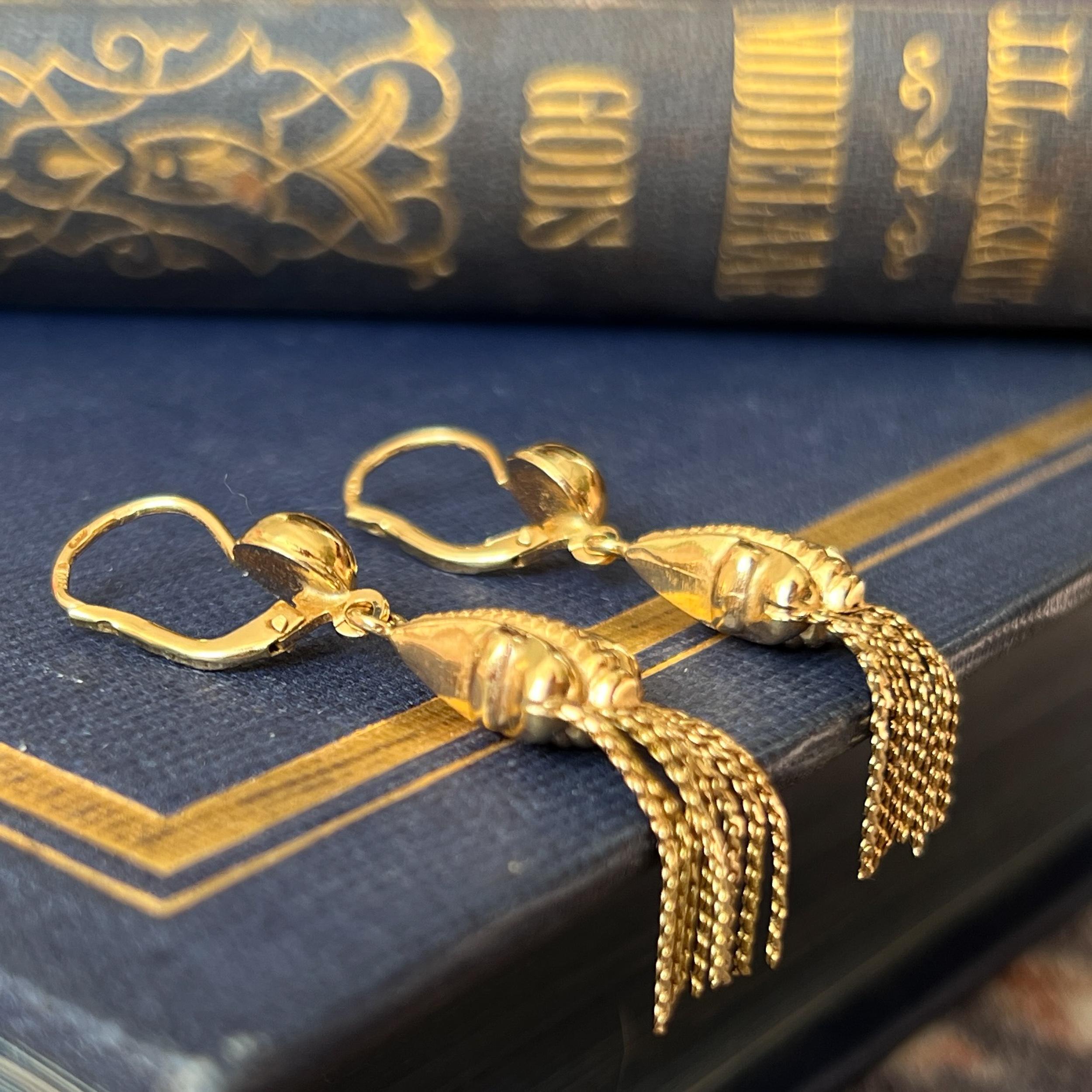A pair of Art Deco tassel dangle earrings created in 18 karat yellow gold. The earrings are beautifully detailed with a scrolling design on the front and back side. The gold is embellished with vertical ribbed motifs in the center. Below the top the