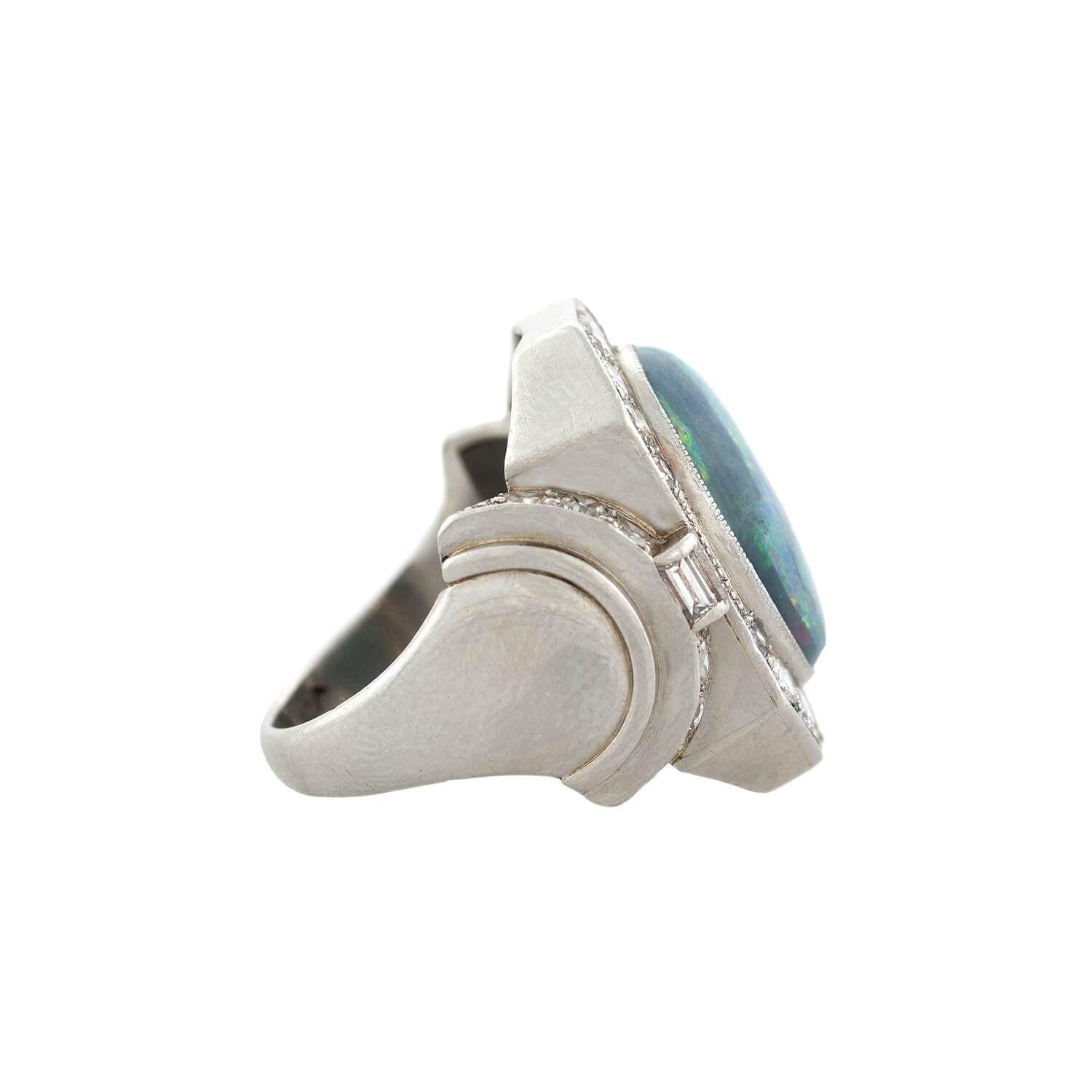 A statement ring from the Art Deco (ca1940s) era! Crafted in 18kt white gold, a Black Opal cabochon rests within a bezel setting. The opal emits an array of rainbow flashes, primary blue and green with bright flecks of red and yellow. The opal's