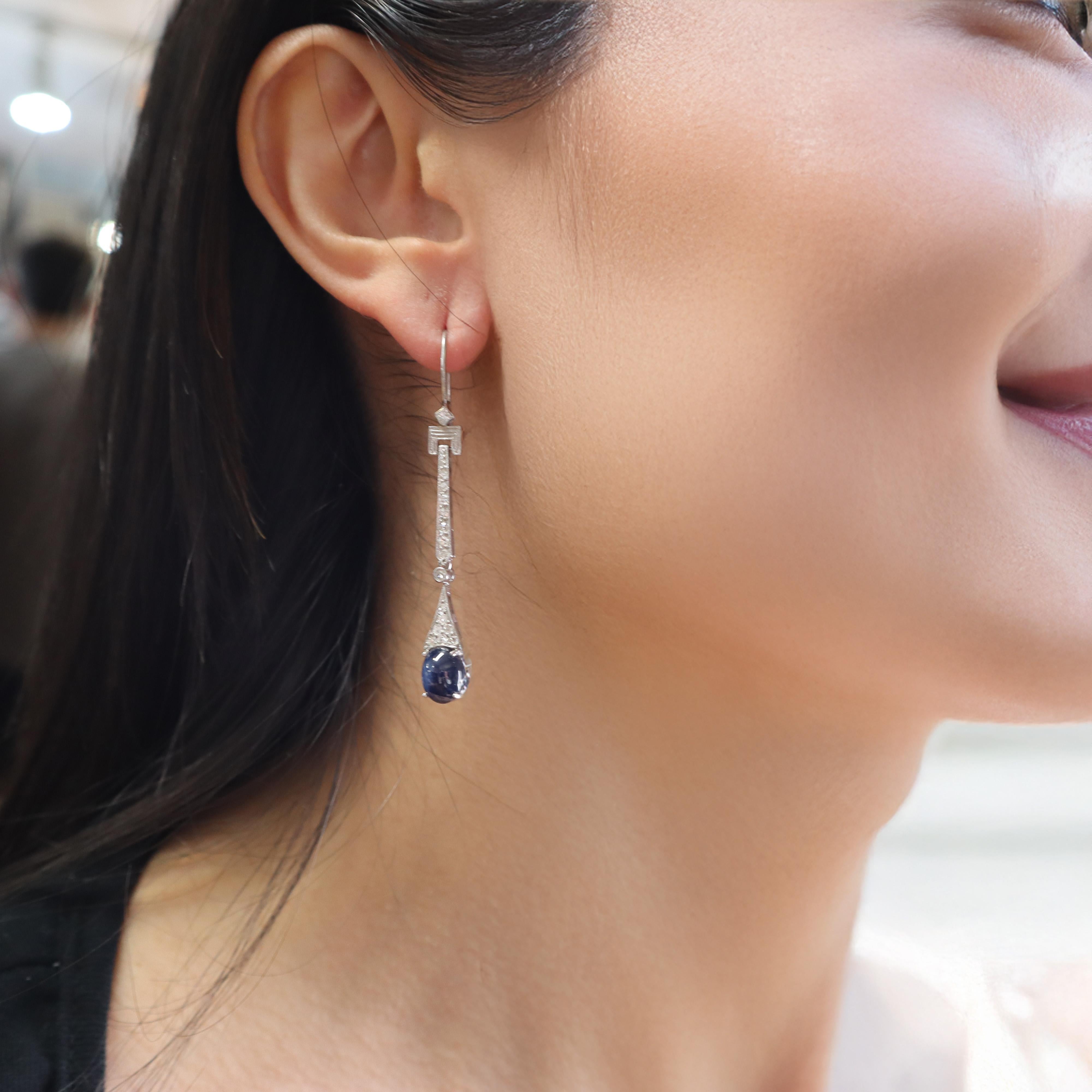 Questo elegante paio di orecchini pendenti è realizzato in platino e presenta un'armoniosa miscela di pietre preziose. Ogni orecchino presenta un affascinante zaffiro blu tagliato a cabochon, con un peso totale di circa 5,0 carati. Questi zaffiri