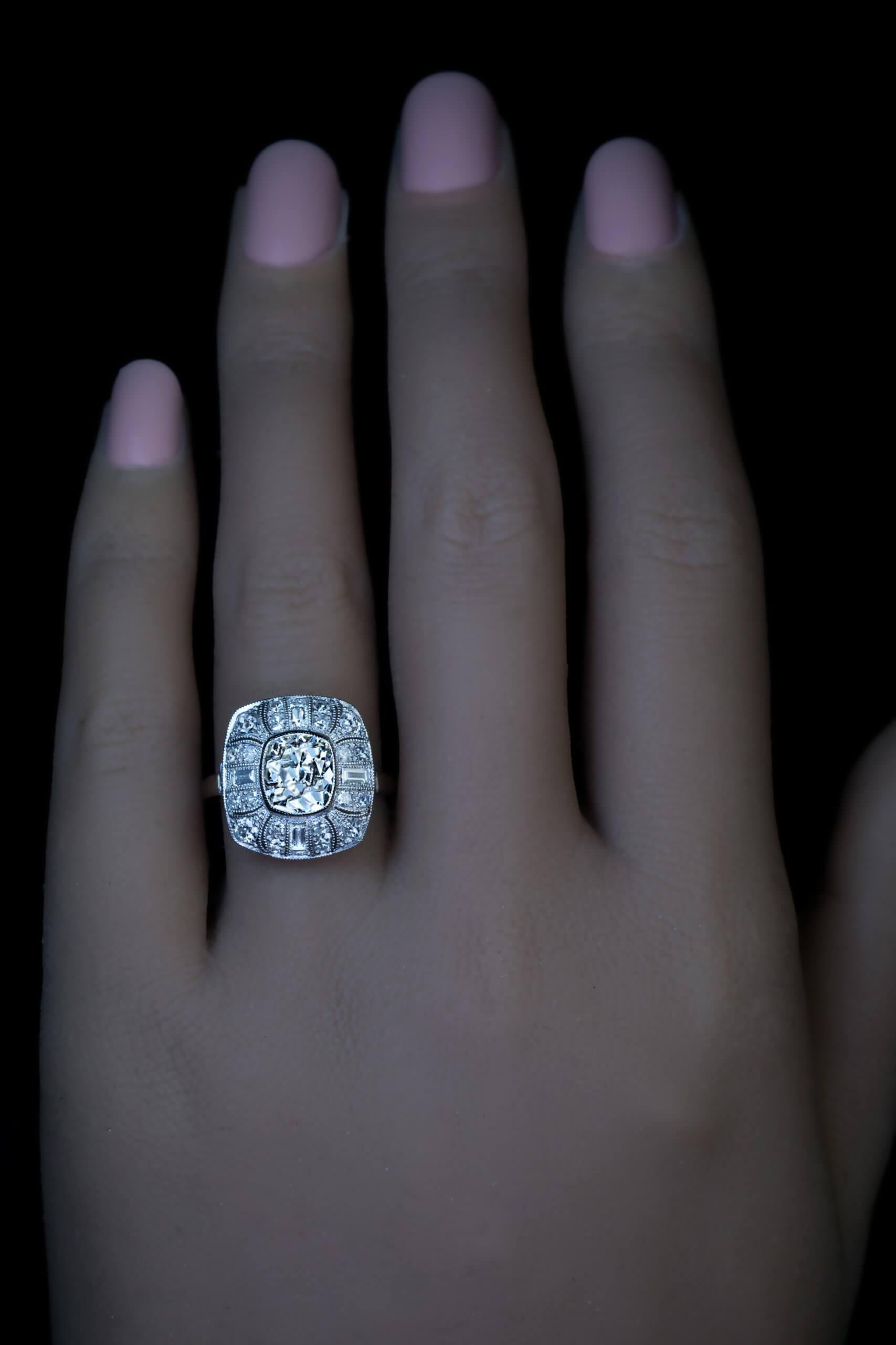 1920s

Dieser Art-Déco-Ring aus Platin mit Maserung hat eine quadratische Form mit abgerundeten Ecken und einer erhabenen Mitte in Form eines stilisierten Blütenkopfs. Der Ring ist mit einem strahlenden alten Diamanten im Kissenschliff (7,6 x 6,8 x
