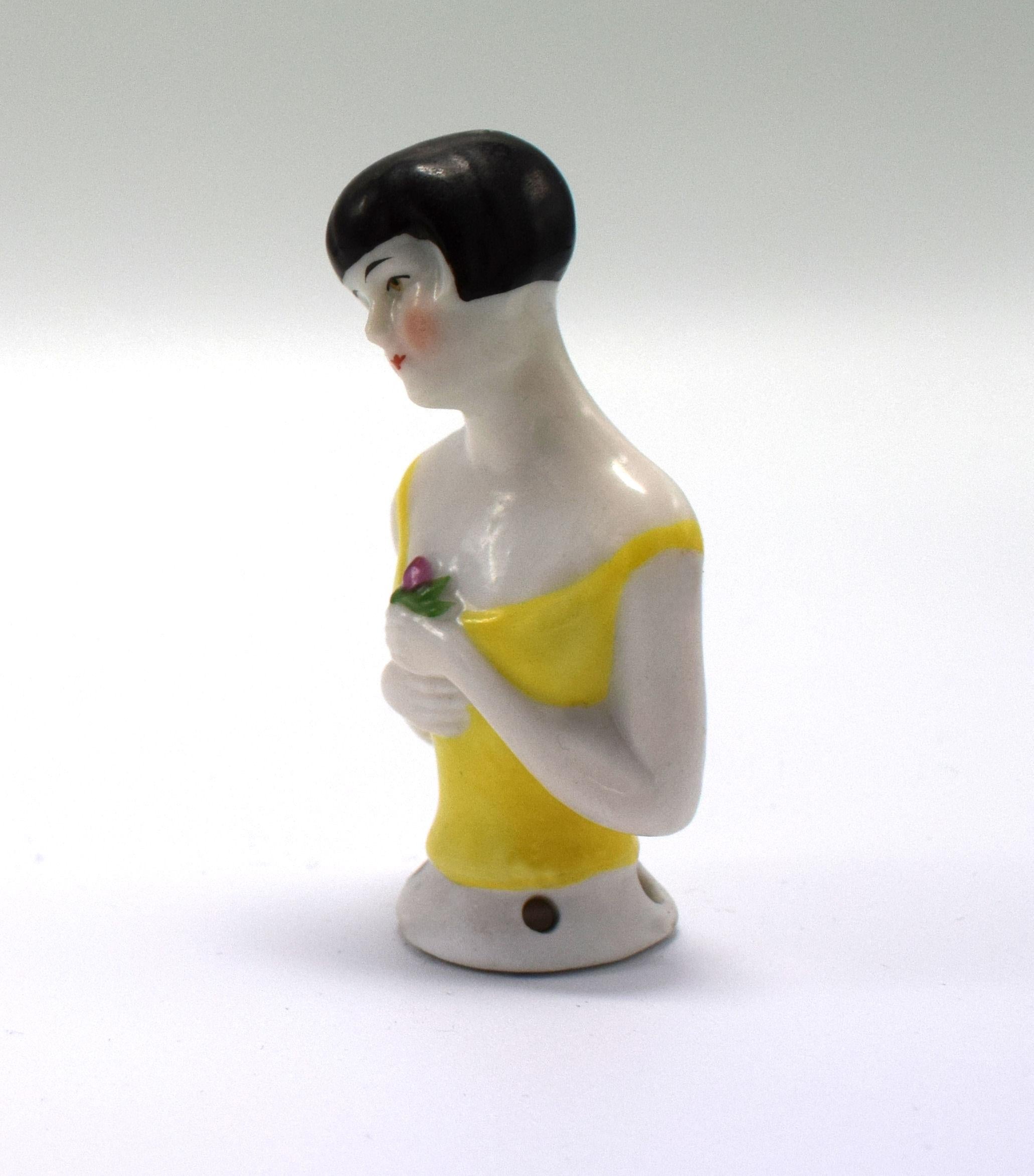 On offer and for your consideration is this charming and totally authentic late 1920s Art Deco German porcelain pin cushion half doll in the form of a pretty flapper girl with a black bob hair cut. She's wearing a daffodil yellow shoestring top with