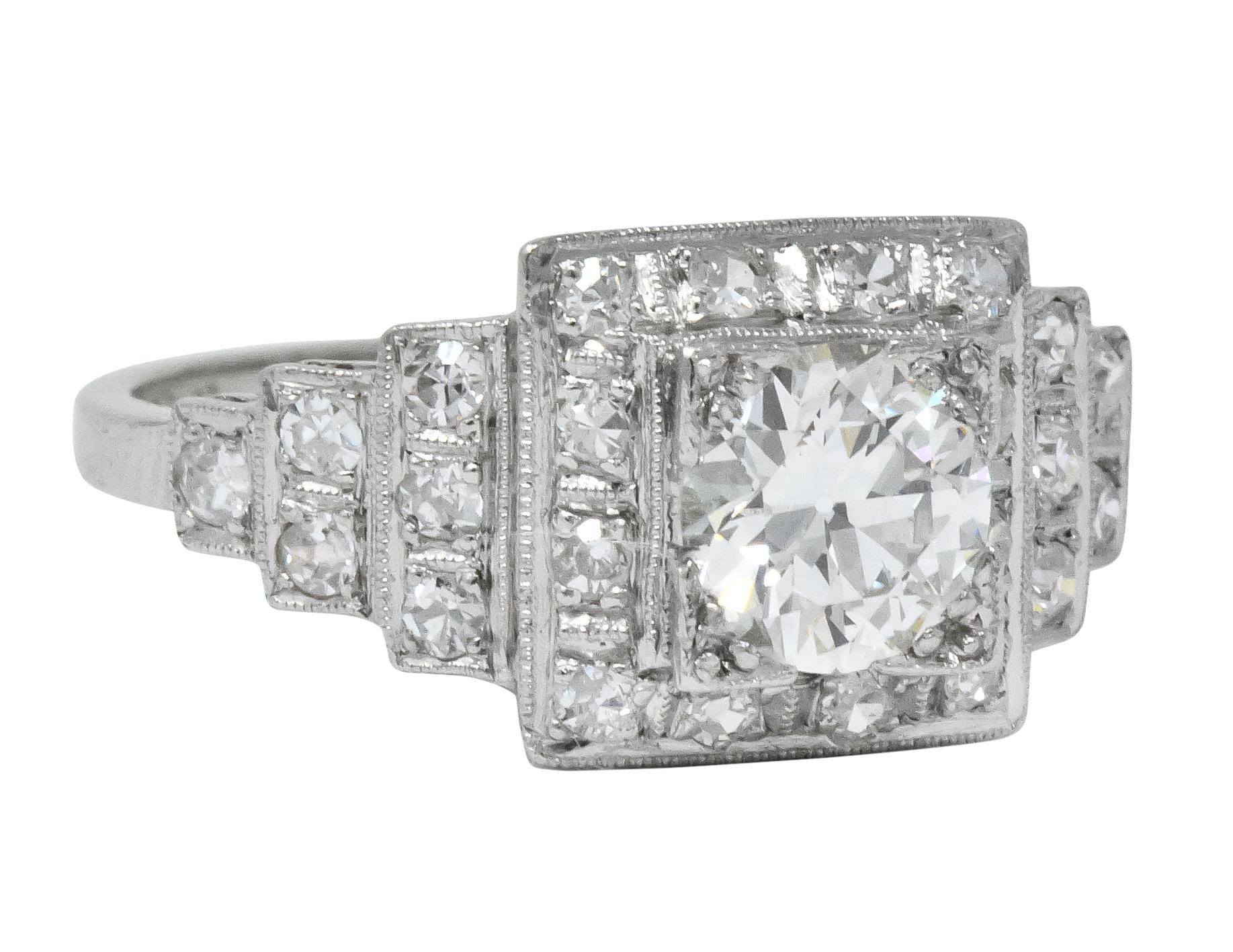 Centering a square form head set with a round brilliant cut diamond weighing 0.84 carat, J color and VS1 clarity

Surrounded by millegrain halo and flanked by deco style stepped shoulders, bead set with single cut diamonds weighing approximately