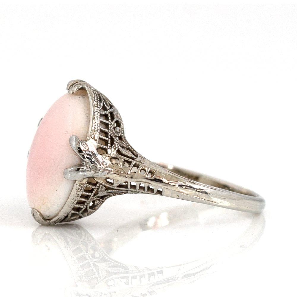 Our 1930s angel skin coral 14ct white gold lace ring, an enchanting piece that embodies the allure and sophistication of the illustrious Art Deco era. This remarkable ring showcases a mesmerising angel skin coral cabochon, renowned for its ethereal
