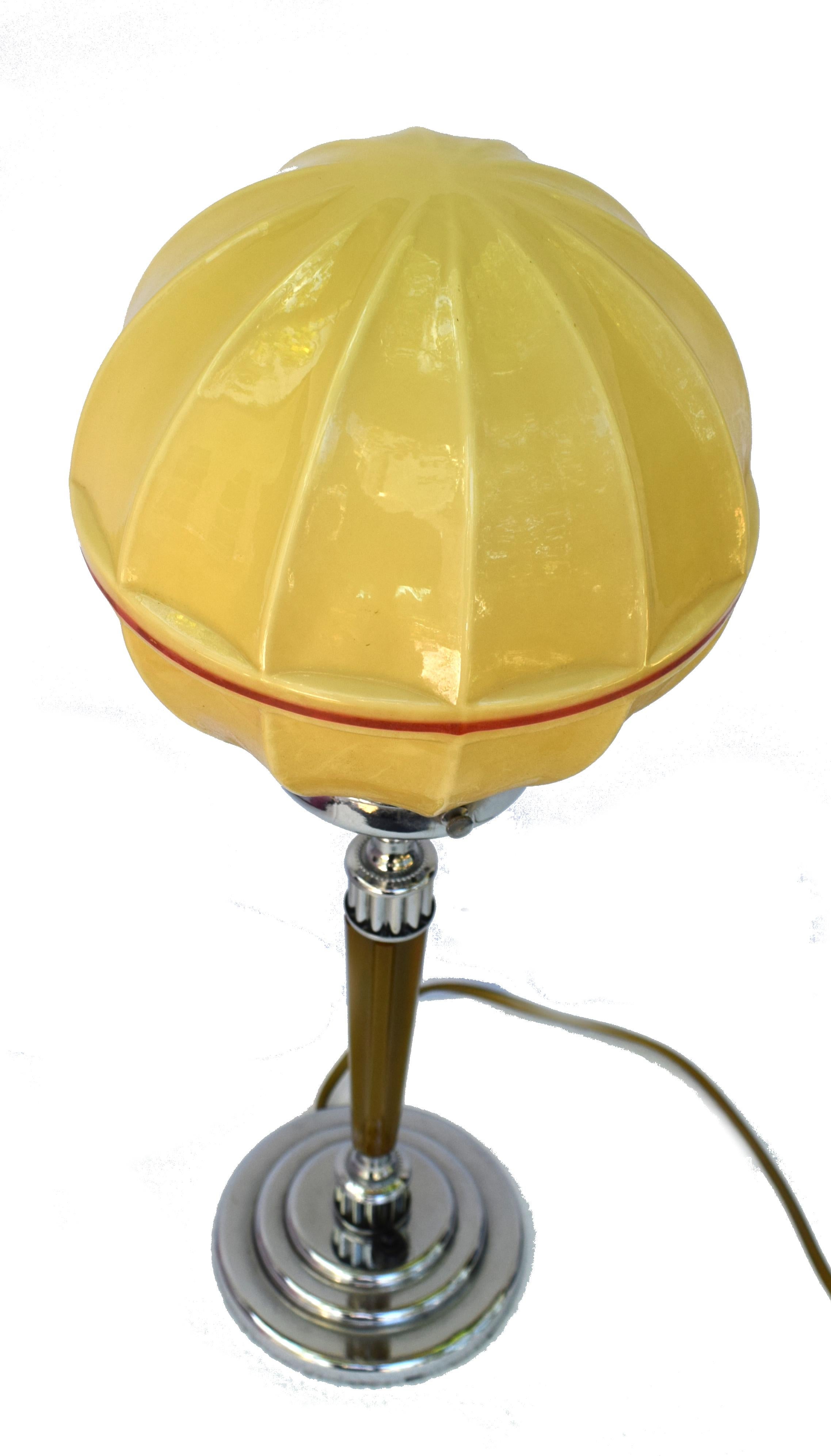 Jolie lampe de table Art Déco des années 30 avec une tige en bakélite cataline à côtes caramel. La base est étagée et circulaire en chrome, ce qui s'équilibre avec le col et la galerie en chrome. Cette lampe est dotée d'un abat-jour en verre de