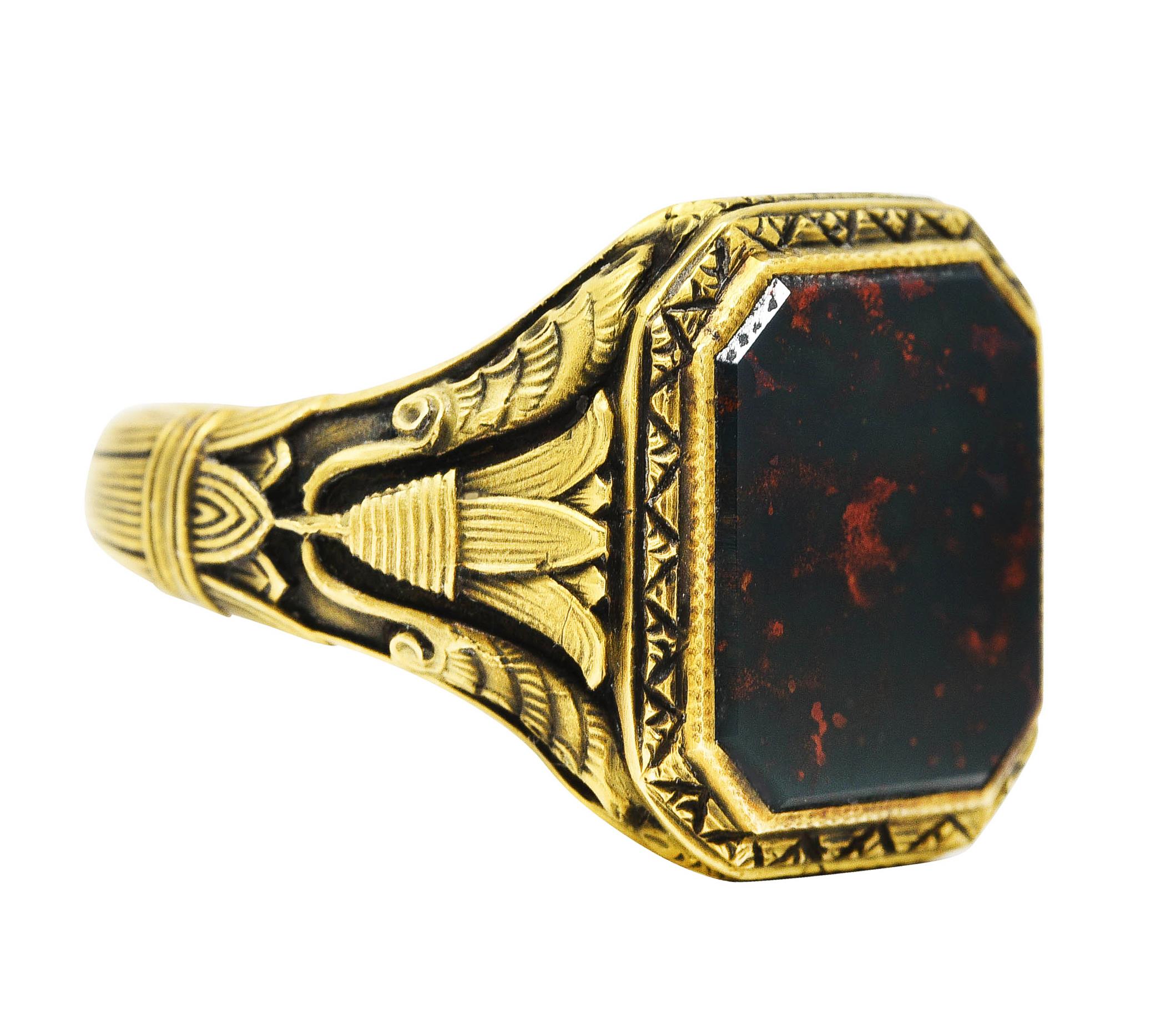Signet style ring with octagonal head and stylized shoulders

Centering an octagonal slab of bloodstone measuring 13.0 x 11.0 mm

Bloodstone is opaque blueish-green with strong orangey red mottling

With geometric patterned surround

Featuring