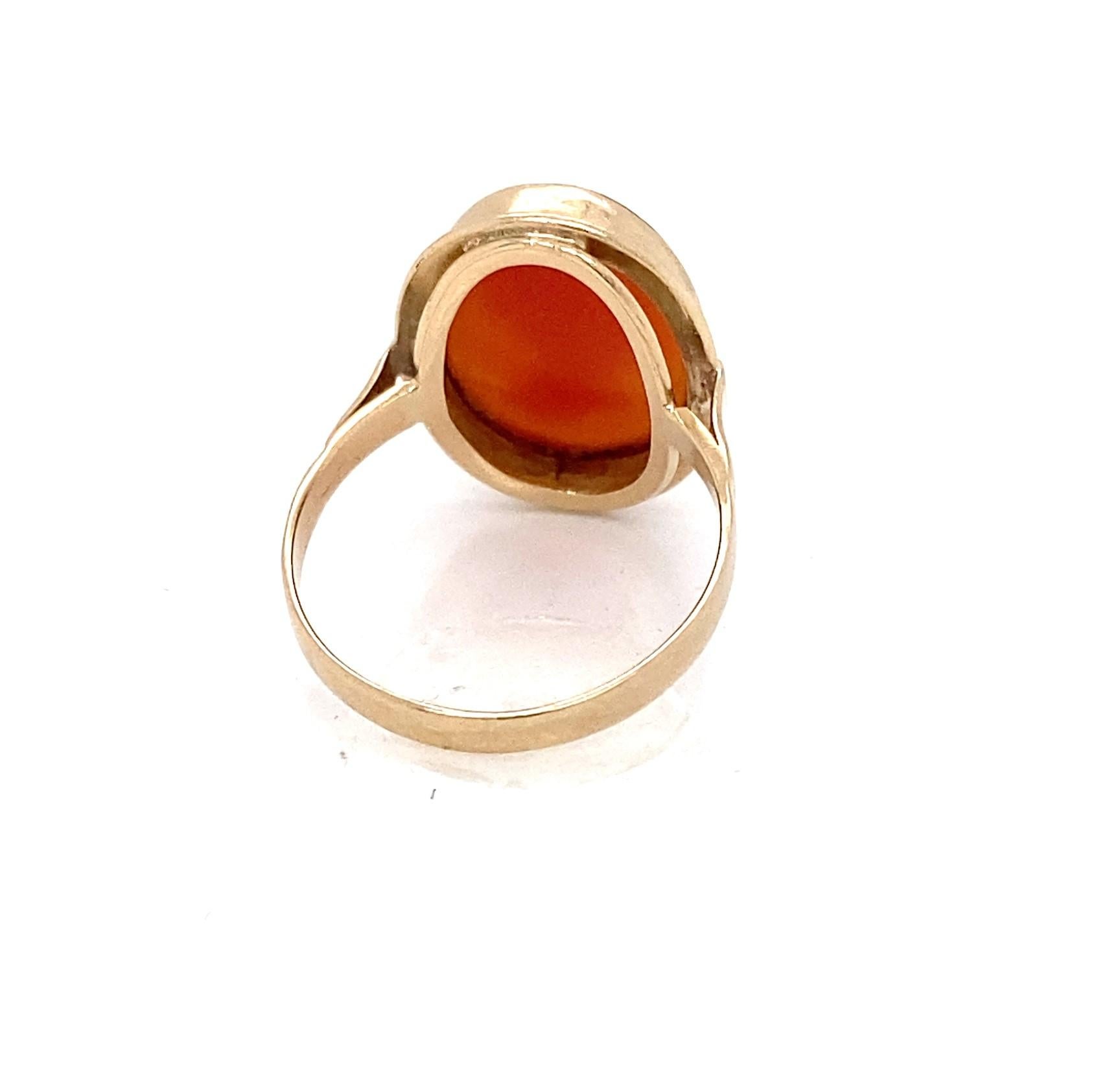 Dieser geschichtsträchtige Ring aus den 1930er Jahren zeigt eine ovale Muschelkamee, die eine Frau im Profil mit Blumen im Haar darstellt.  Die Kamee ist in eine Lünette aus 14-karätigem Gelbgold gefasst, die den sittsamen Gesichtsausdruck der Frau