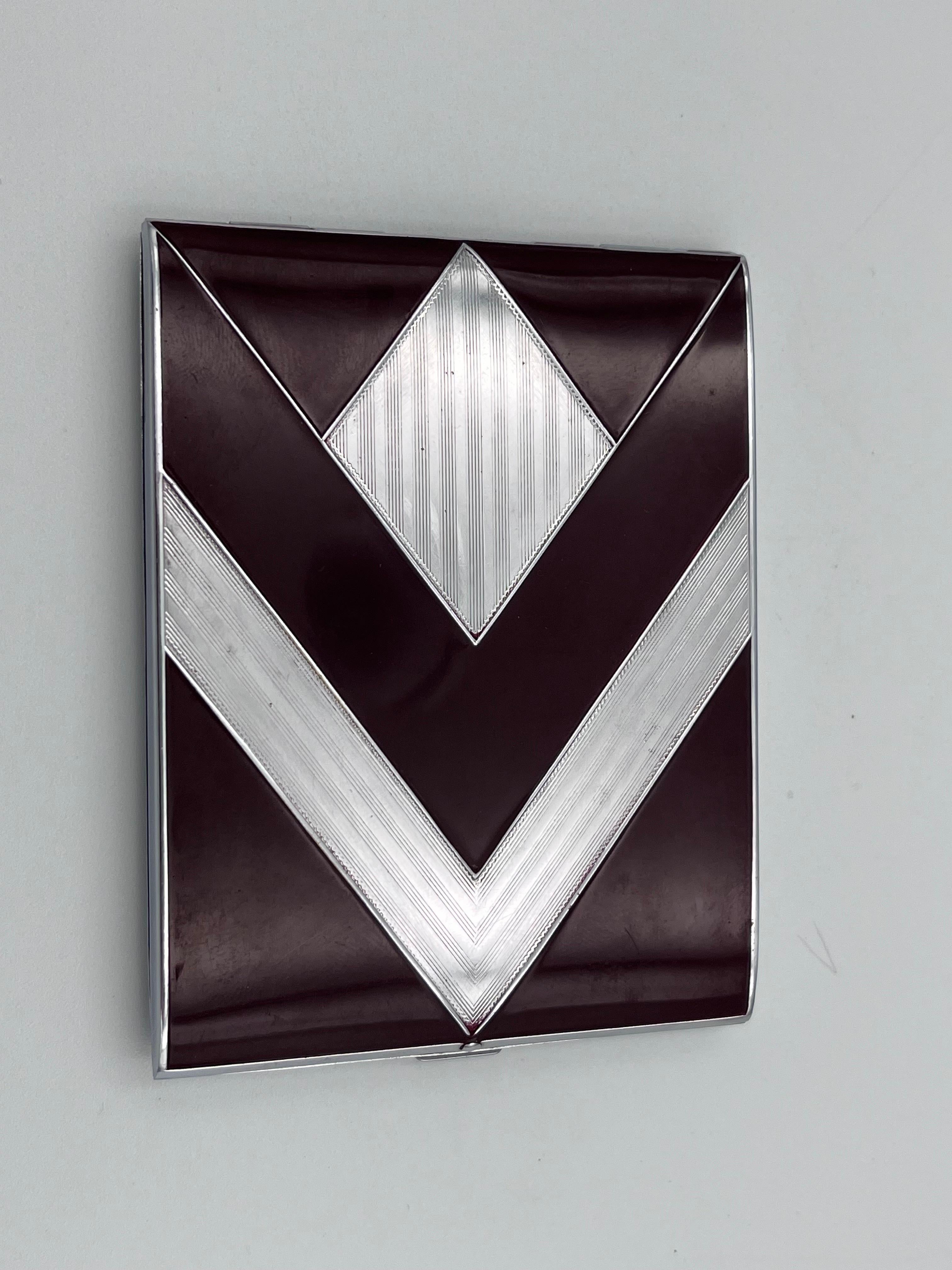 Questo favoloso portasigarette Evans degli anni '30 sfoggia una delle combinazioni più sorprendenti dell'epoca: audaci motivi chevron e diamante resi in cromo scintillante e ricco smalto bordeaux sangue di bue. Il contrasto tra i toni profondi dello