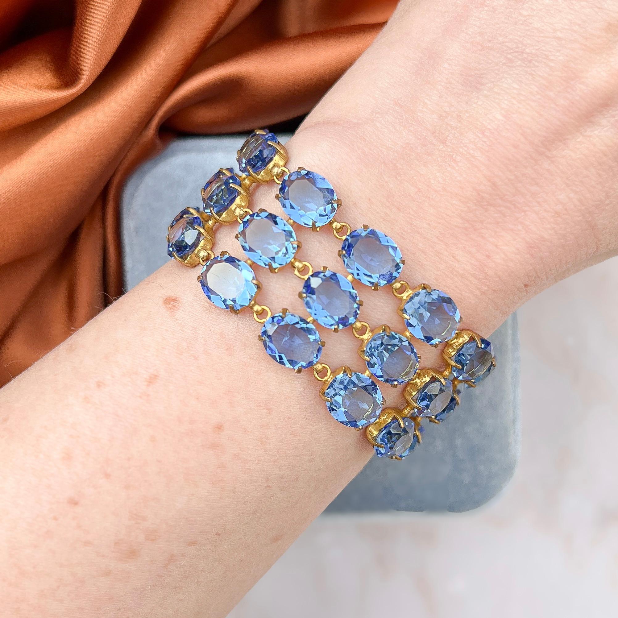 This stylish bracelet dates from the 1930s. It was most likely created in Czechoslovakia. 

Condition Report:
Excellent 

The Details...
This gilded metal bracelet features three rows of oval cut, multi-faceted, claw set and open back mounted blue
