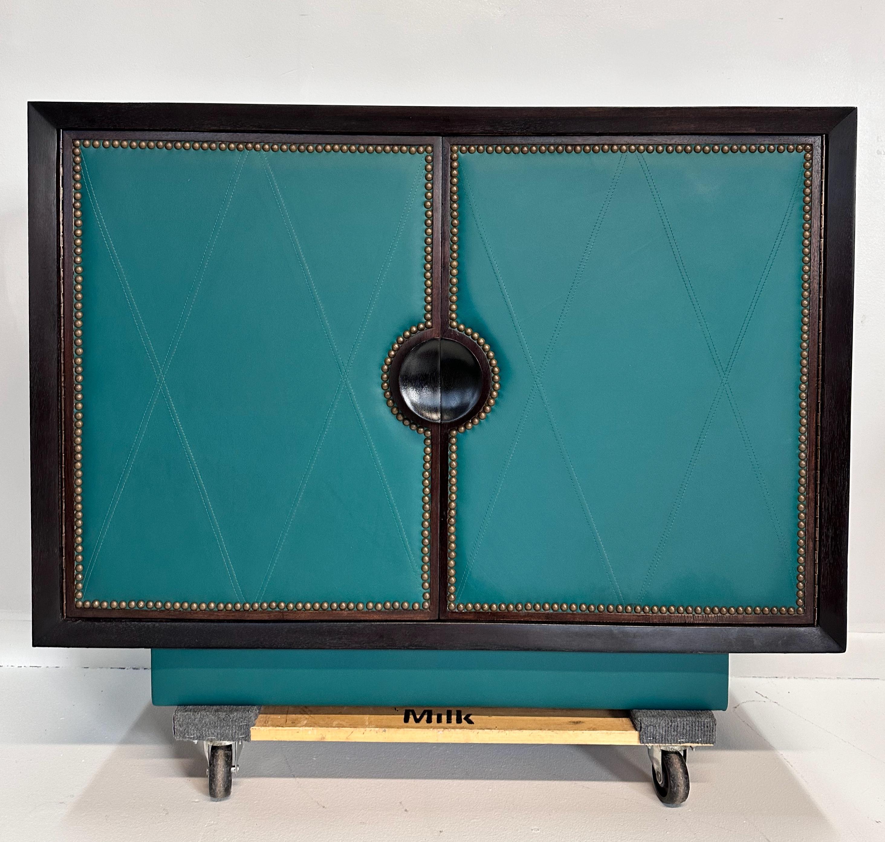 Classic art deco high style mahogany cabinet with tooled and sewn diamond pattern green leather door panels and distinctive polished brass tacks. Features three large spacious drawers and two small top drawers.

Beautifully restored.