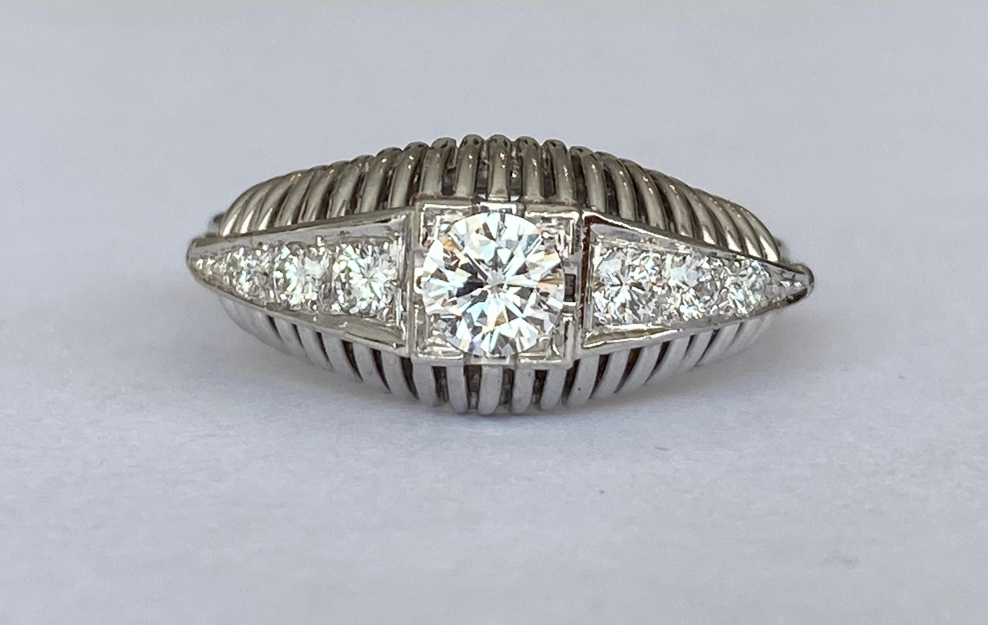 The 18 kt gold  ring is an authentic vintage diamond engagement ring from the Late  Art Deco era, circa 1940's. This ring features an 0.34 carat brilliant cut  diamond of H color and VS2 clarity, flanked by six (6) brilliant cut diamonds approx.