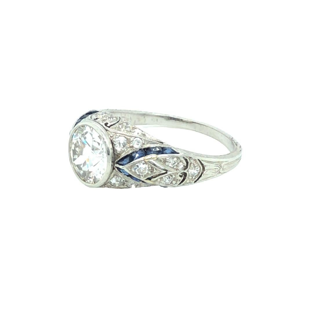 An elegant Art Deco diamond and sapphire platinum engagement ring. This Art Deco piece is right in between the Art Deco and Edwardian Era. Featuring a 2 carat F color, VVS2 clarity, bezel set Old European cut diamond accented on either side by