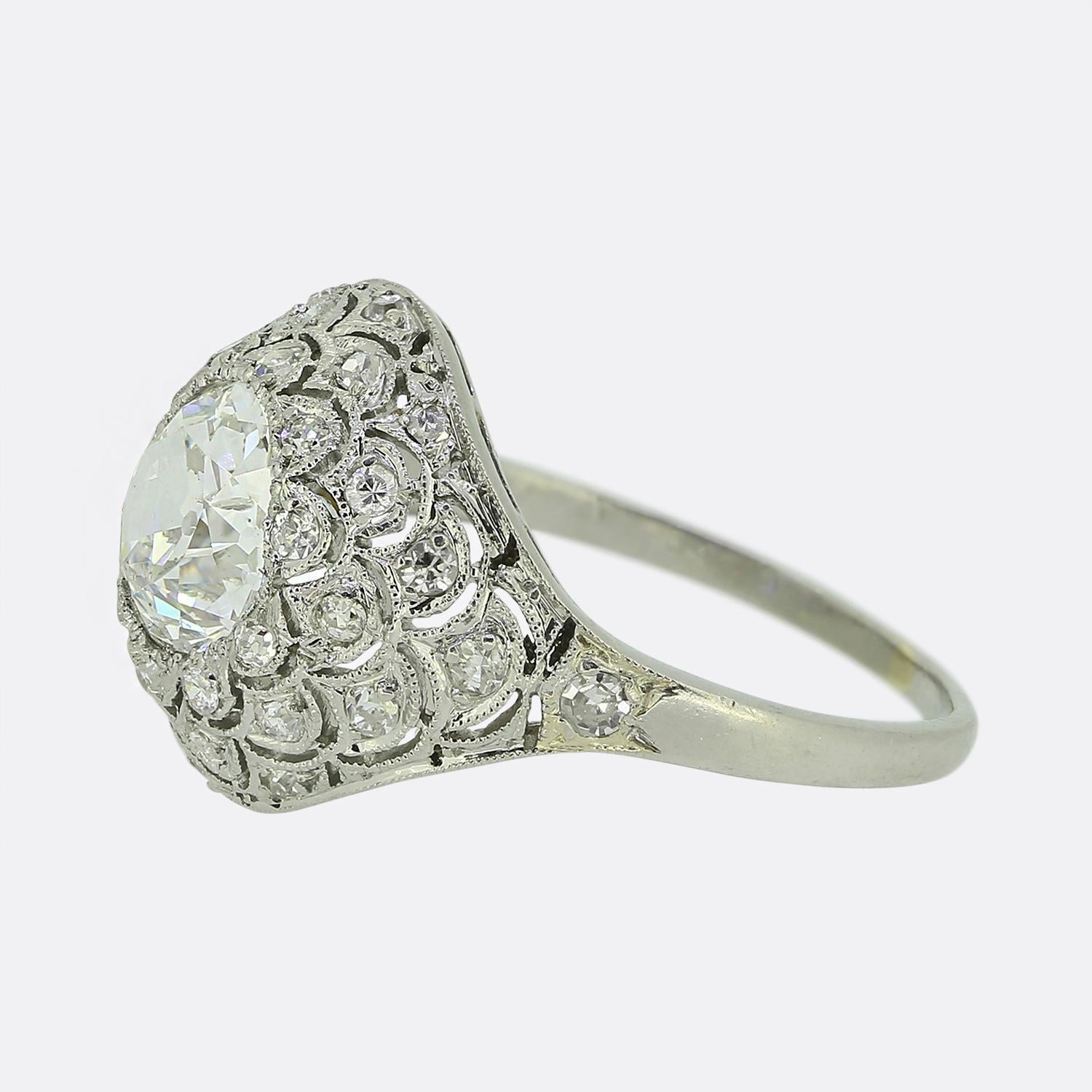 Here we have an exquisite Art Deco ring. At the centre of the face we find a prominent 2.00ct round faceted old mine cut diamond radiating a captivating white hue whilst being securely set within an intricate millegrain setting; a detailing which