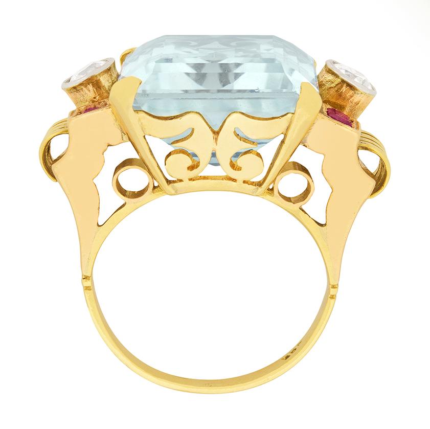 This amazing 20.00 aquamarine cocktail ring was created in the 1920s. It is a lovely blue colour, and is an emerald-cut. There are two 0.40 carat old cut diamonds on either side, that are G colour and SI clarity.  Four 0.15 carat baguette cut rubies