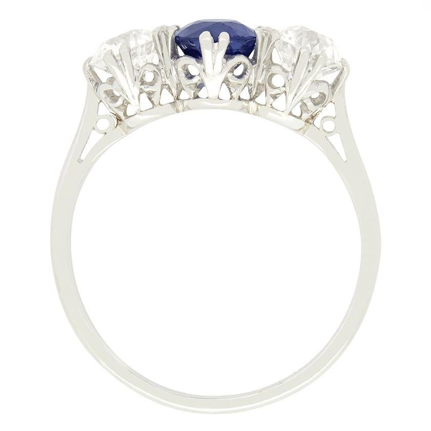 An intense royal blue Sapphire sits between two old cut diamonds in this timeless Art Deco trilogy ring. The natural unheated sapphire is an oval cut stone weighing 2.00 carat. The flanking diamonds are 0.50 carat a piece matching in quality at F in