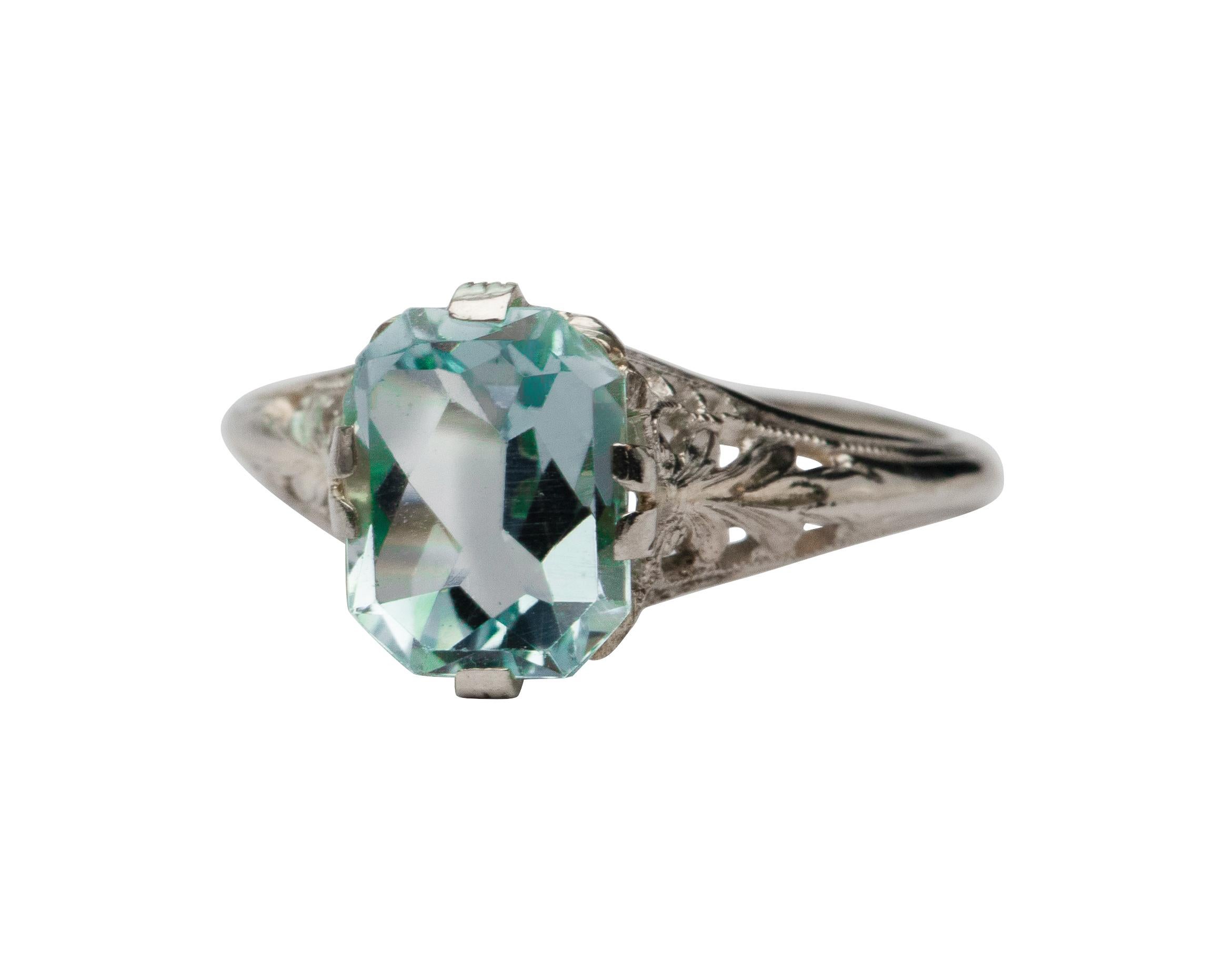 This lovely art deco aquamarine ring is a fantastic example of a turn of the century fashion piece. The beautiful pastel blue shade of the aquamarine shines in the intricate filigree white gold mounting. A delicate array of pierced designs accented