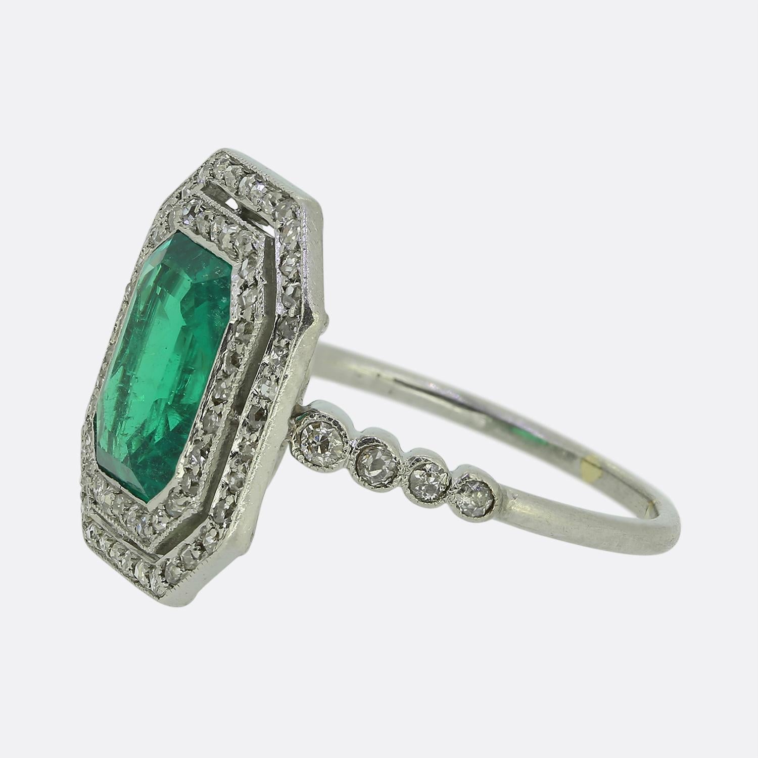 Ecco un raffinato anello a grappolo in platino realizzato durante l'apice del movimento Art Déco. Al centro si trova uno smeraldo tagliato a smeraldo, con una vibrante tonalità di verde, saldamente incastonato in una faccia geometrica. Intorno a