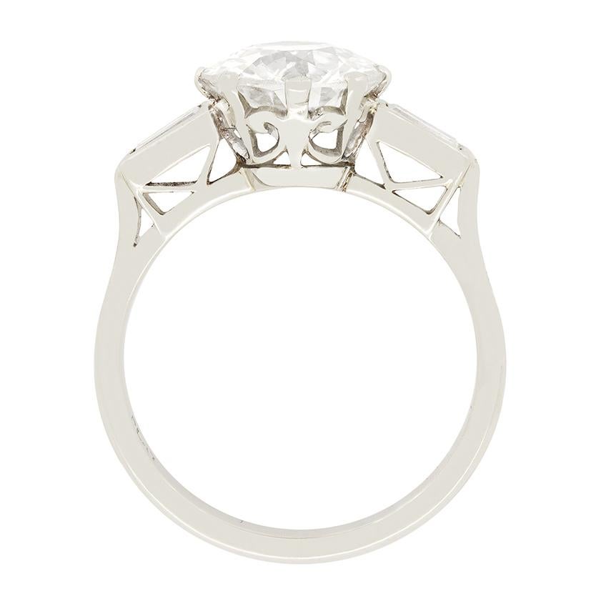 This timeless art deco solitaire ring features a 2.10 carat old cut diamond at its centre. The diamond is claw set and has been graded I-J in colour and SI in clarity. Either side of the stunning central stone are a pair of baguette cut diamonds