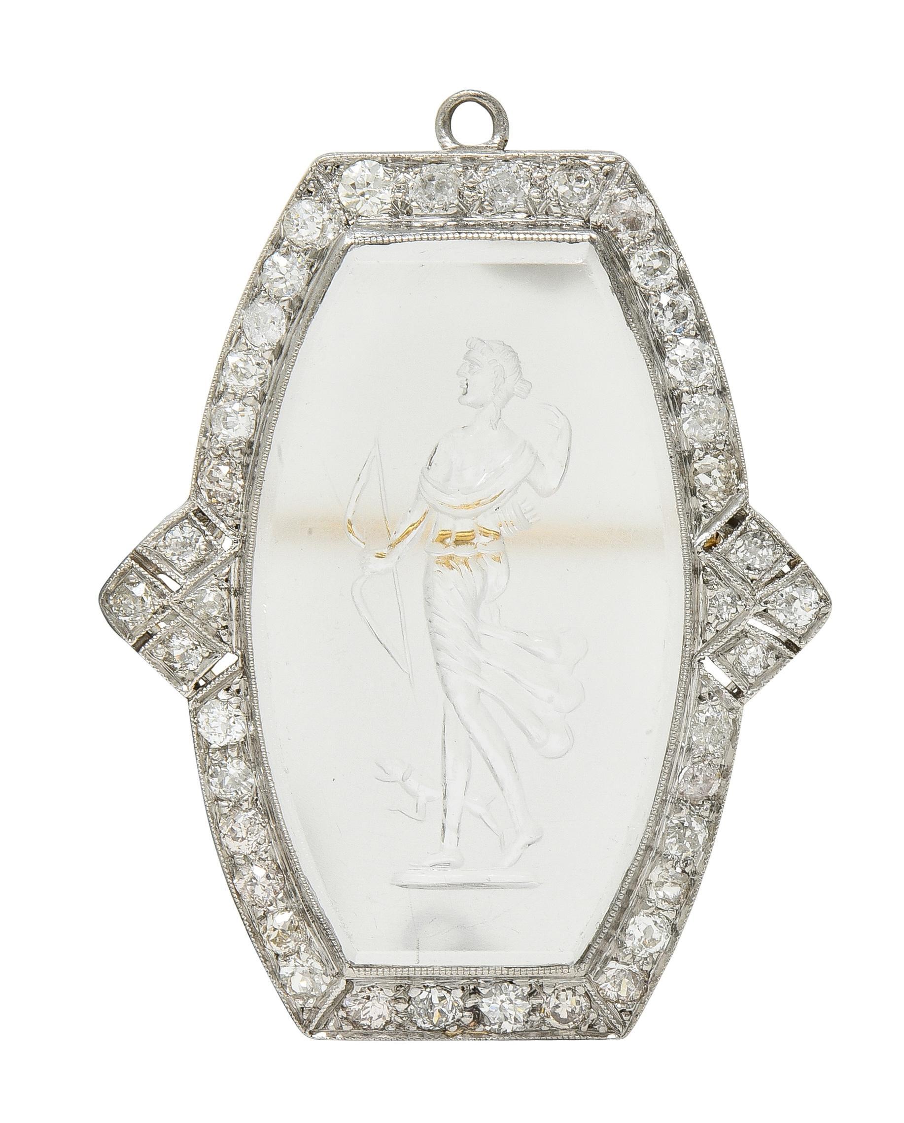 Centering an elongated cushion-shaped tablet of transparent and partially frosted rock crystal 
Carved to depict the Greek goddess Artemis walking with a dog and carrying a bow
Measuring 19.0 x 32.0 mm - set in milgrain bezel with halo