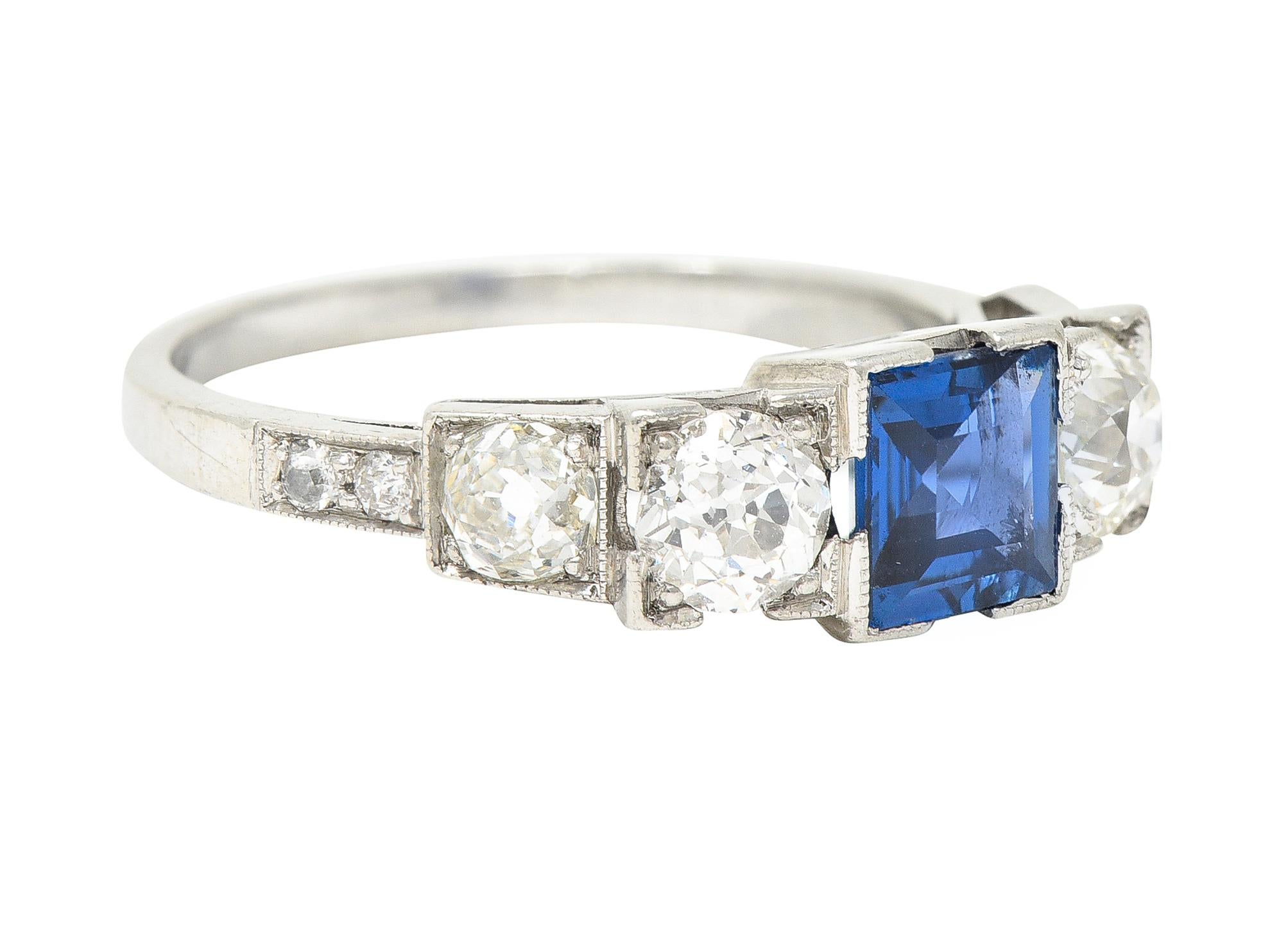 Band ring features five prominent gemstones. Set to front in square form heads and flanked by cathedral shoulders. Centering a square step cut sapphire weighing approximately 1.00 carat. Extremely eye-clean and blue in color with medium saturation.