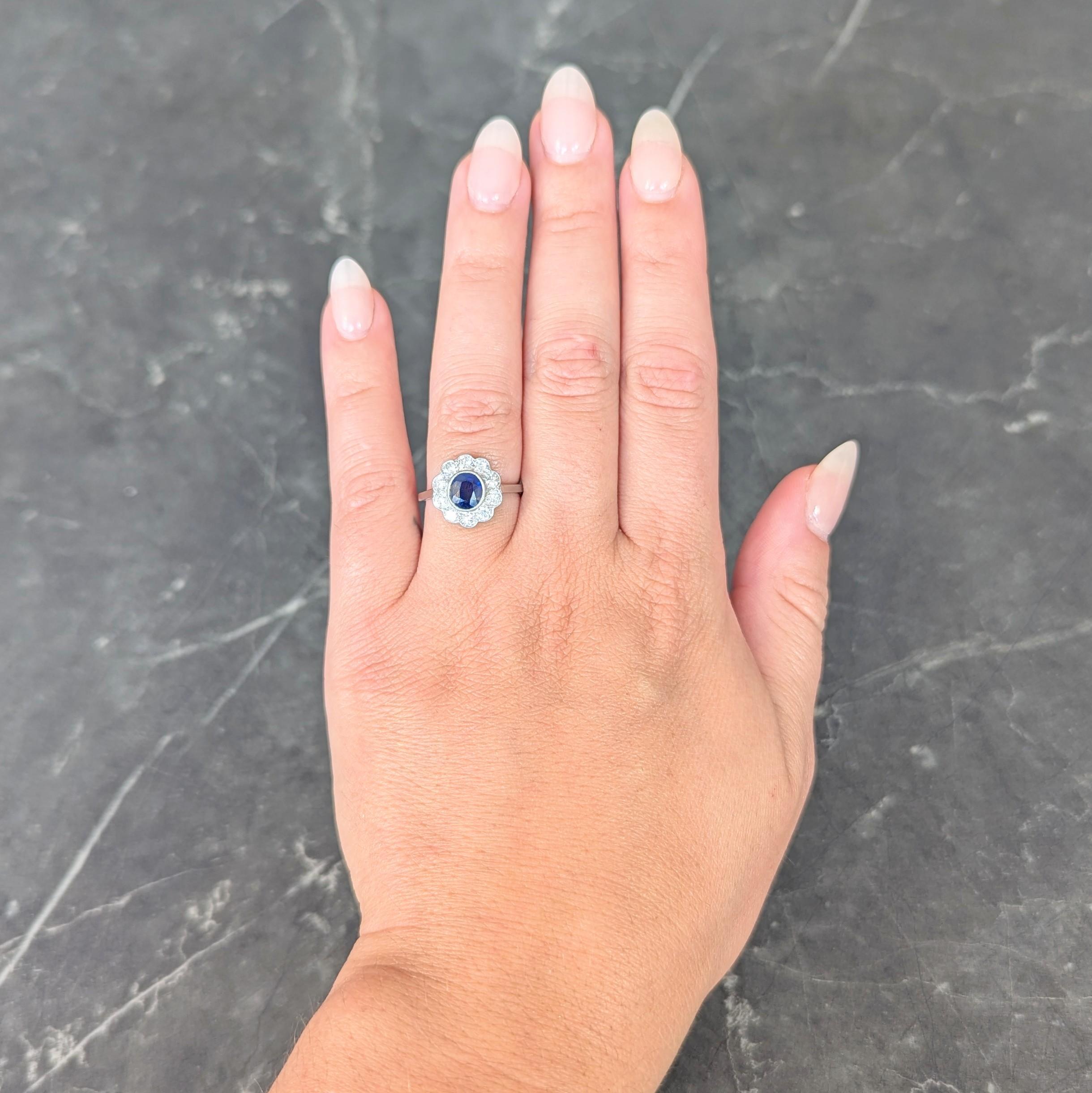 Centering a cushion cut sapphire weighing approximately 1.35 carats
Transparent medium blue in color - bezel set with milgrain detail
Accented by an old European cut diamond halo surround
Weighing approximately 0.80 carat total 
H/I color with VS2