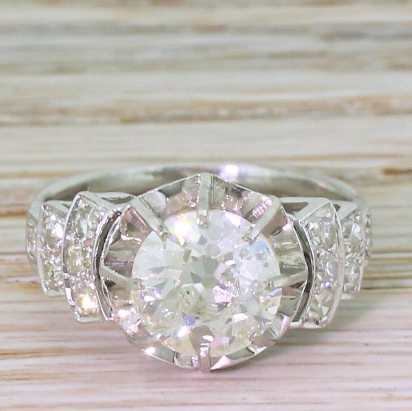 A bold and really rather exceptional Art Deco diamond ring. The old mine cut in the centre is secured in an eight-claw open collet above a finely scalloped and mirrored back plate. Fine detailing in the gallery leads to wide, statement shoulders