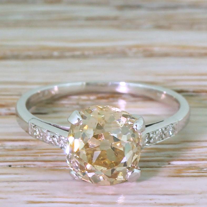 A stunning and unique antique diamond ring. The cushion shaped old cut diamond displays a distinct and bright orangey brown hue and is secured in a four claw collet with fine geometric detailing in the gallery. Six (three each side) small eight cut