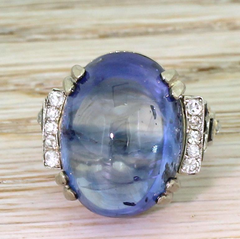 A monumentally beautiful ring. The large cabochon sapphire in the centre – certified as natural, without heat treatment and originating from Ceylon – is secured by four split claws in a simple double gallery. The sapphire is complemented by