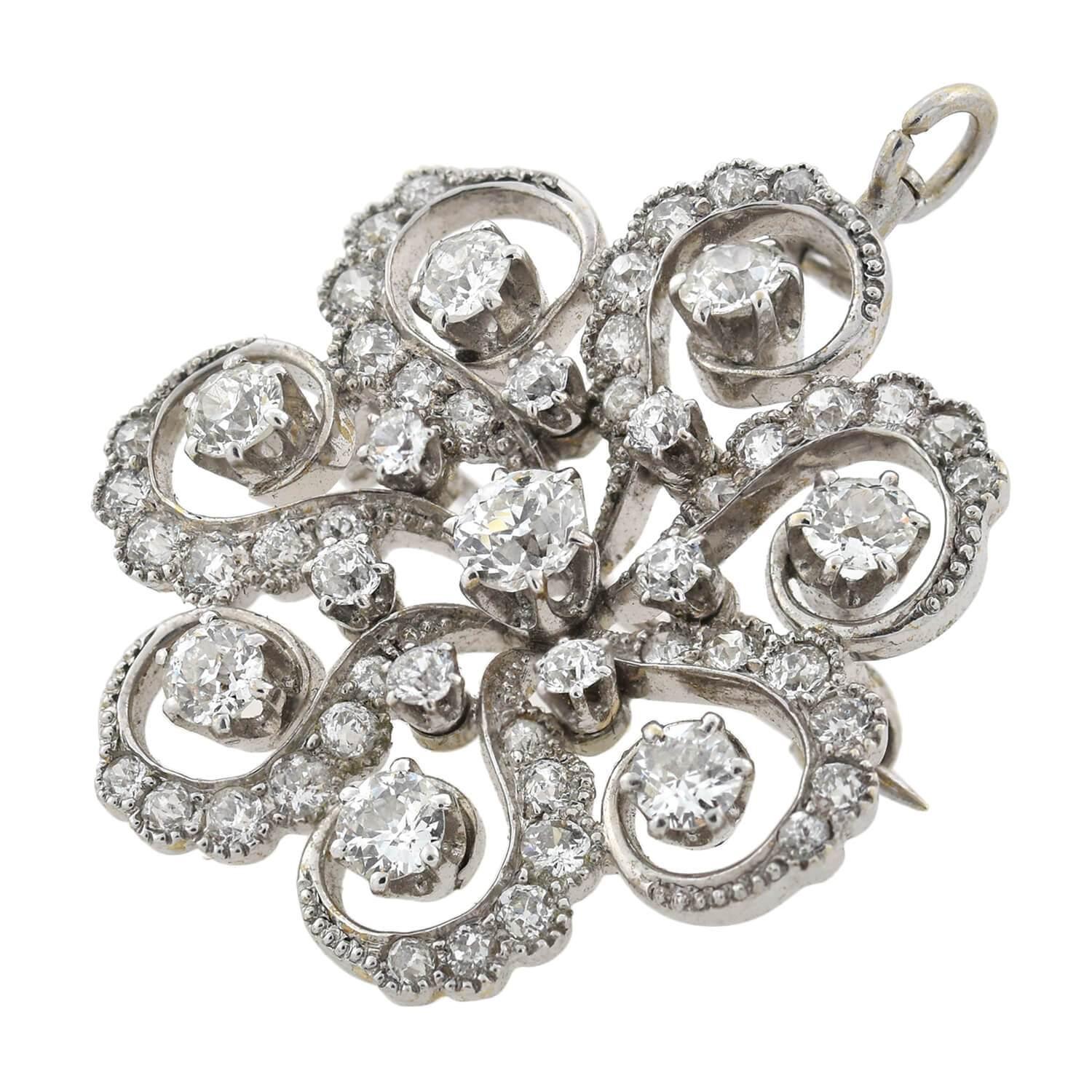 A beautiful diamond encrusted pin/pendant from the late Art Deco (ca1930s) era! This stunning piece is crafted in rhodium plated 18kt gold and forms the unique shape of a swirled floral motif decorated with sparkling diamonds. Seven beautiful old