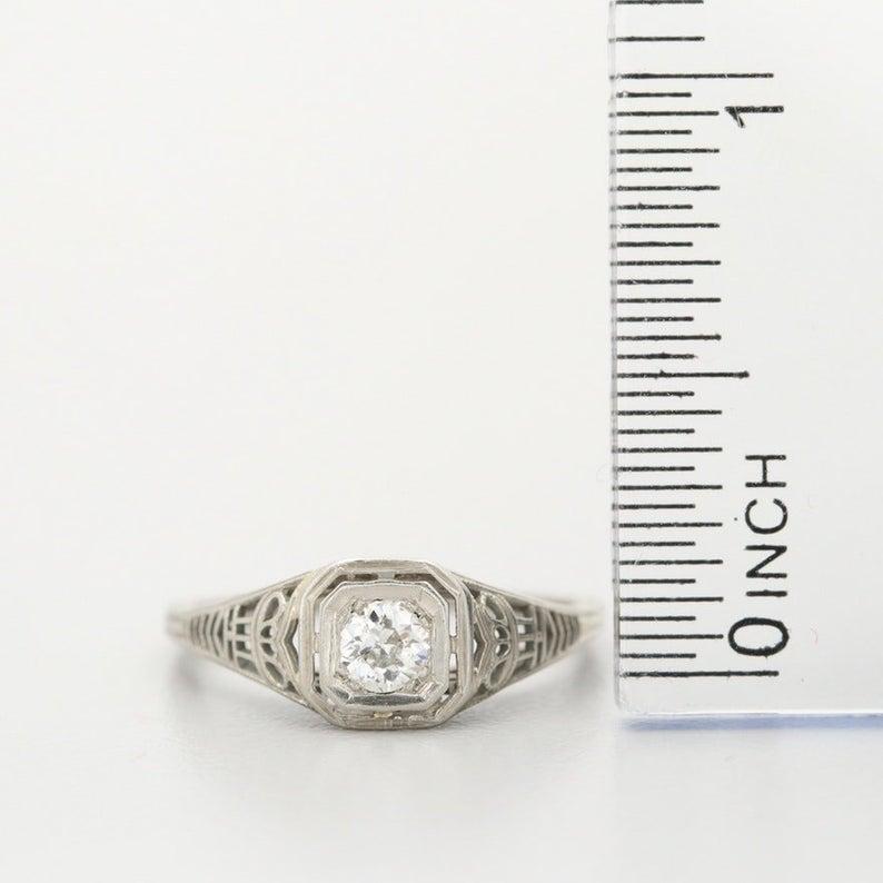 Description: 
Here we have a genuine 1920's Art Deco diamond ring crafted in 18 karat white gold. The sparkling .25 carat old cut diamond is held by a beautiful intricate filigree mounting. 

This is a true antique piece, and we are honored to offer