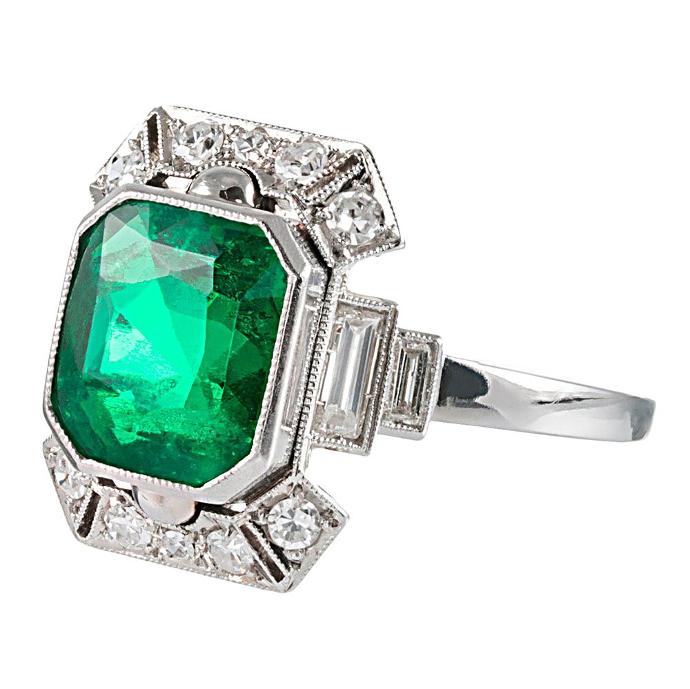 Intricate art deco architecture encircles a 2.50 carat emerald. Boasting striking color and excellent transparency, the stone sits protected in its platinum bezel and complimented by round- and baguette white diamonds. The diamonds weigh
