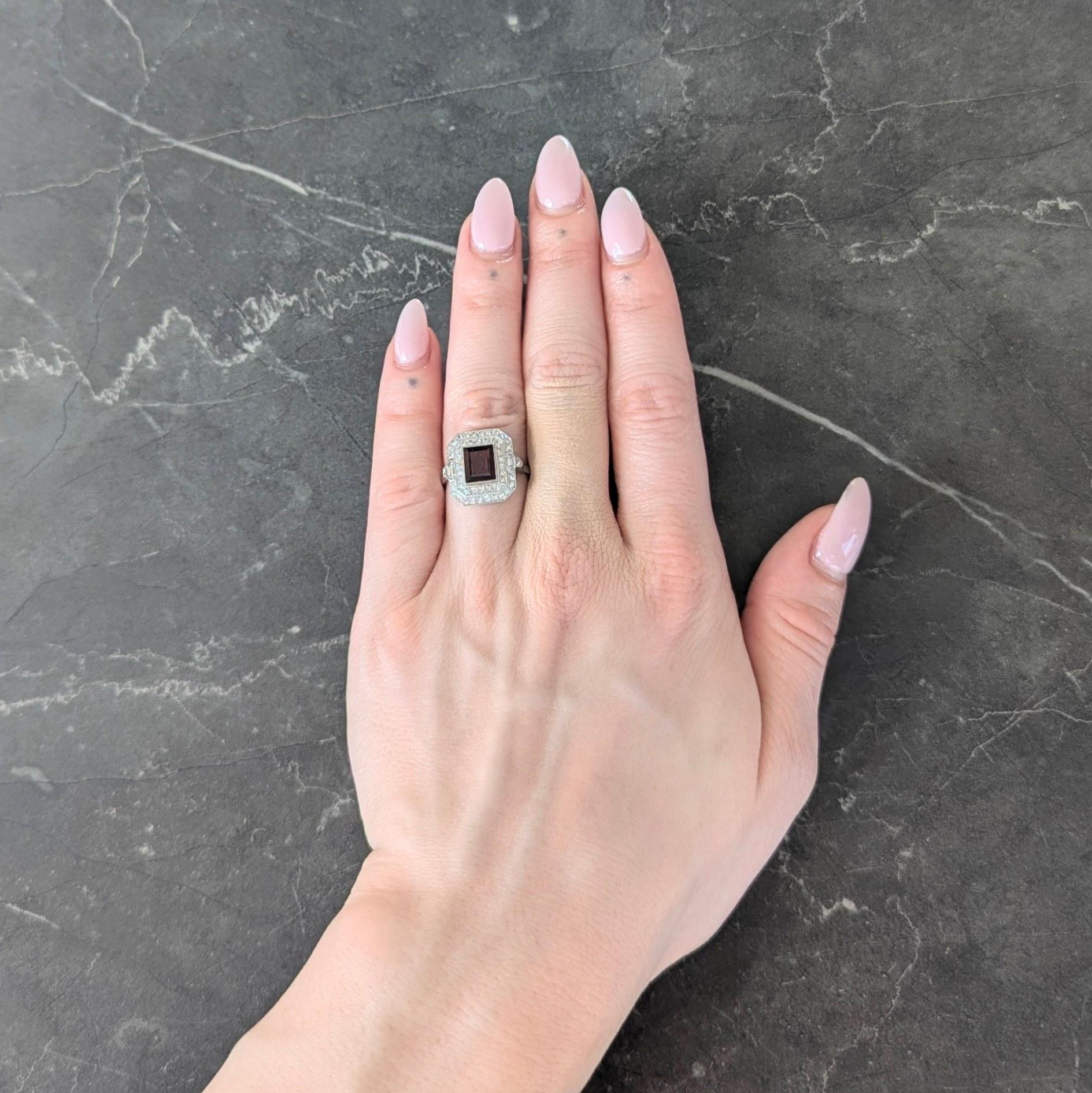 Centering a rectangular step-cut garnet weighing approximately 1.55 carats total - transparent brownish red in color
Set by milgrain bezel a with a bead set double halo surround of single cut diamonds
With additional bezel set hexagonal cut diamonds