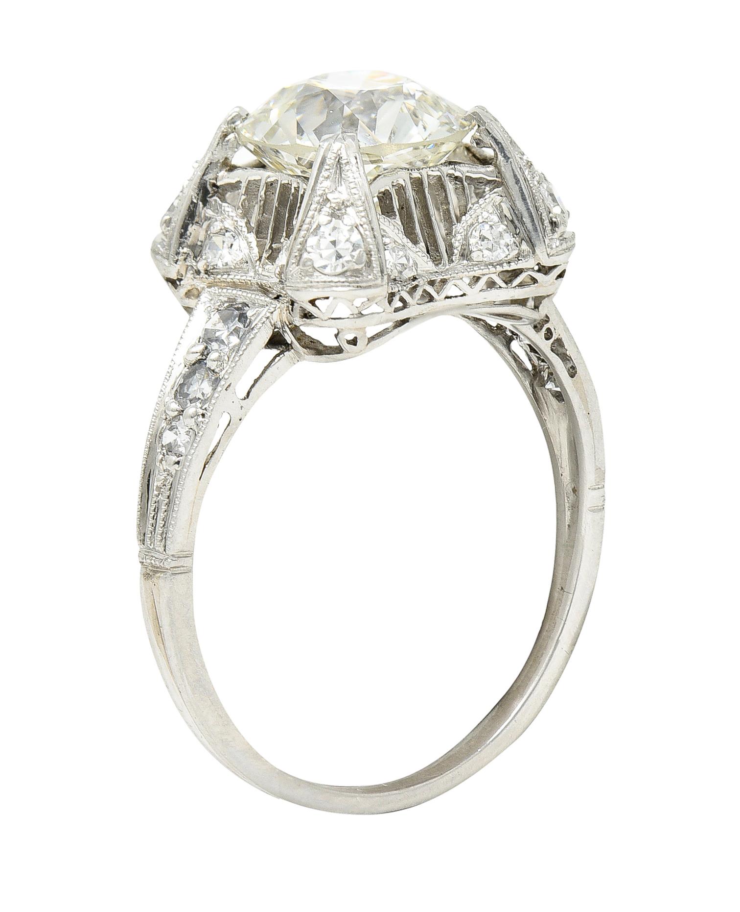 Centering an old European cut diamond weighing approximately 2.13 carats total - K color with VS1 clarity. Set with decorous grooved prongs with milgrain detailing in a cushion shaped surround. Featuring pierced linear detailing with geometric