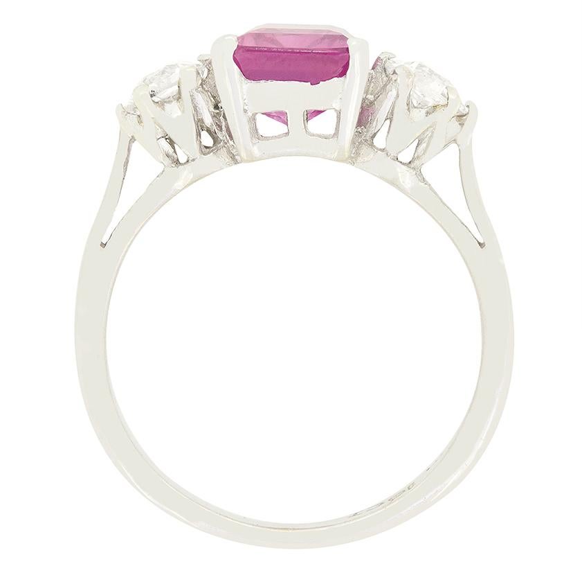 Risalente agli anni '30, questo anello trilogy Art Deco presenta uno splendido zaffiro rosa naturale al centro, affiancato da diamanti taglio vecchio. Lo zaffiro taglio smeraldo pesa 2,60 carati ed è una pietra naturale non riscaldata proveniente da