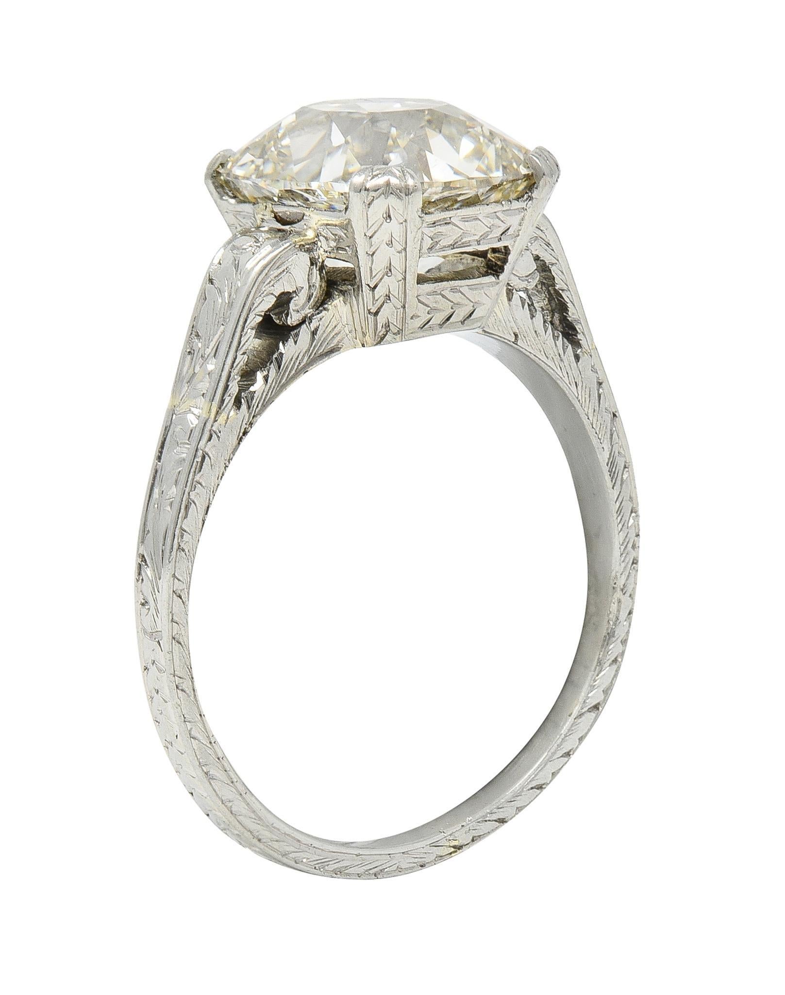 Centering an old mine cut diamond weighing 2.69 carats - M color with SI1 clarity 
Set with wide prongs and a detailed wheat motif engraved basket 
Flanked by scrolling volute shoulders engraved with scroll motif
With engraved wheat motif