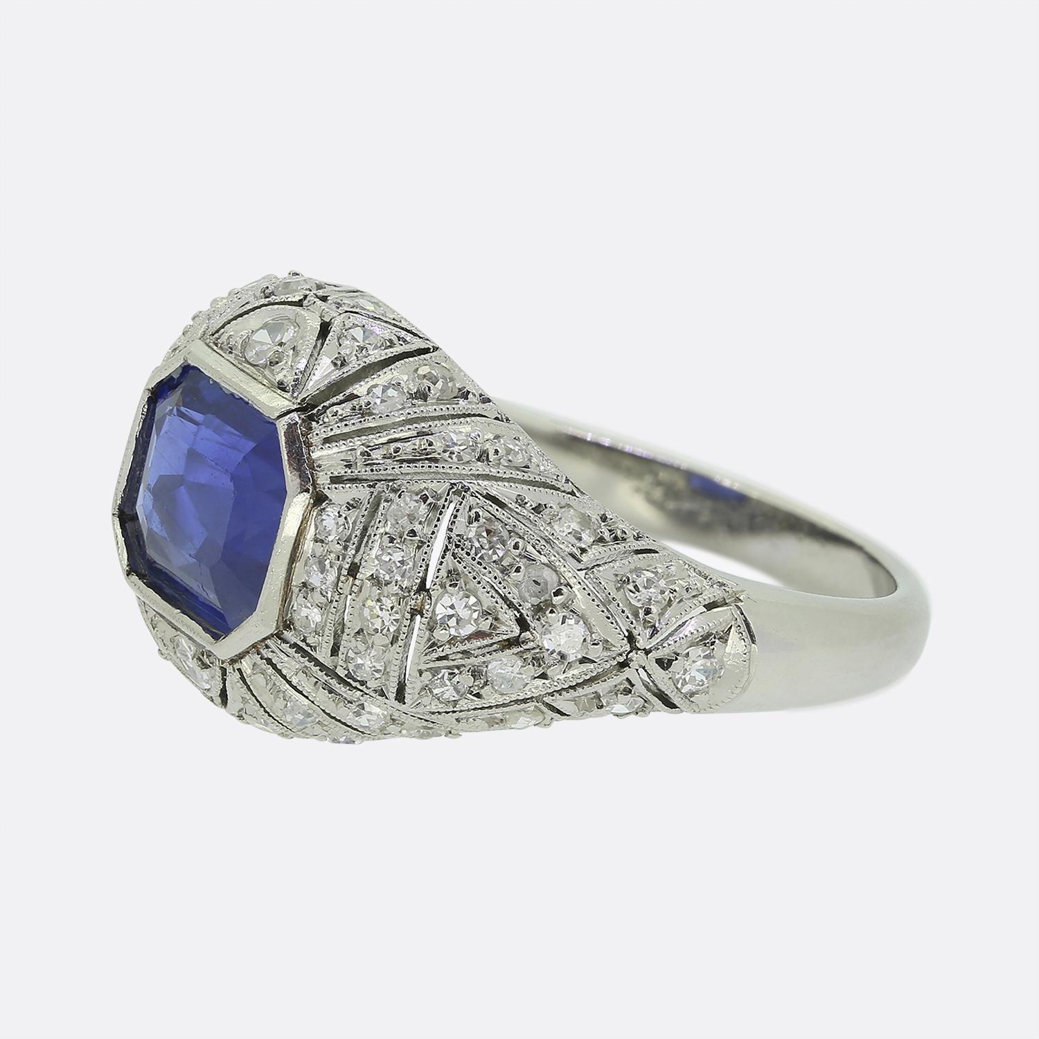 Ecco un delizioso anello a grappolo realizzato durante l'apice del movimento Art Déco. Al centro del quadrante troviamo uno splendido e vibrante zaffiro blu naturale, incastonato in un intricato disegno in filigrana con sottili aperture e raffinati