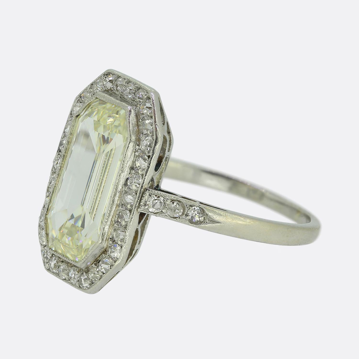 Aquí tenemos un precioso anillo Art Decó en racimo de platino con un diamante talla esmeralda de tamaño considerable en el centro de la cara. Esta piedra primaria se ha tallado de forma única para que parezca una gran mesa, pero en realidad es más