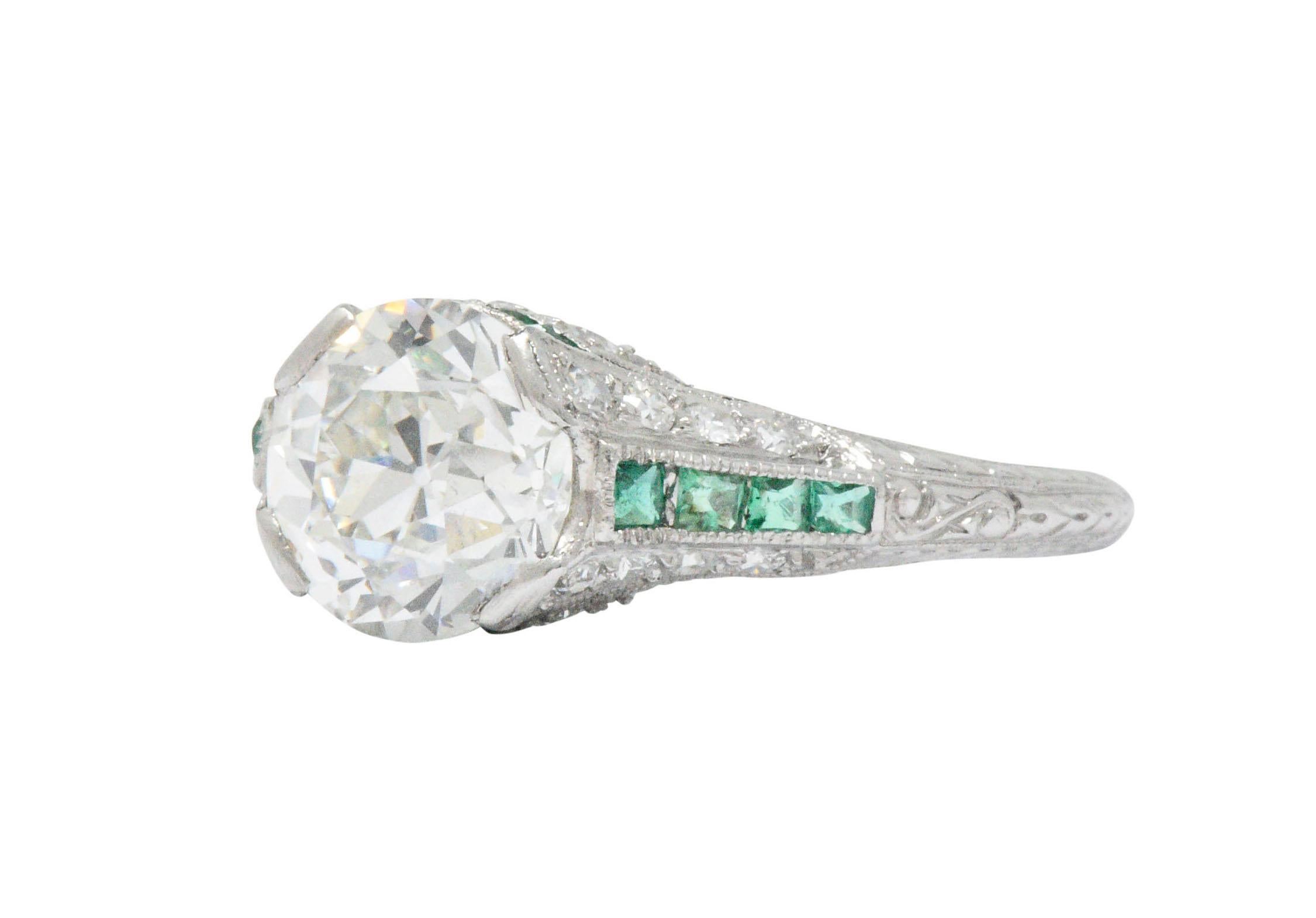 Centering an old European cut diamond weighing 2.05 carats, I color and VS1 clarity, set low in mounting by wide prongs

Channel set at each cardinal point by square cut emeralds weighing approximately 0.35 carat; translucent and verdant green in