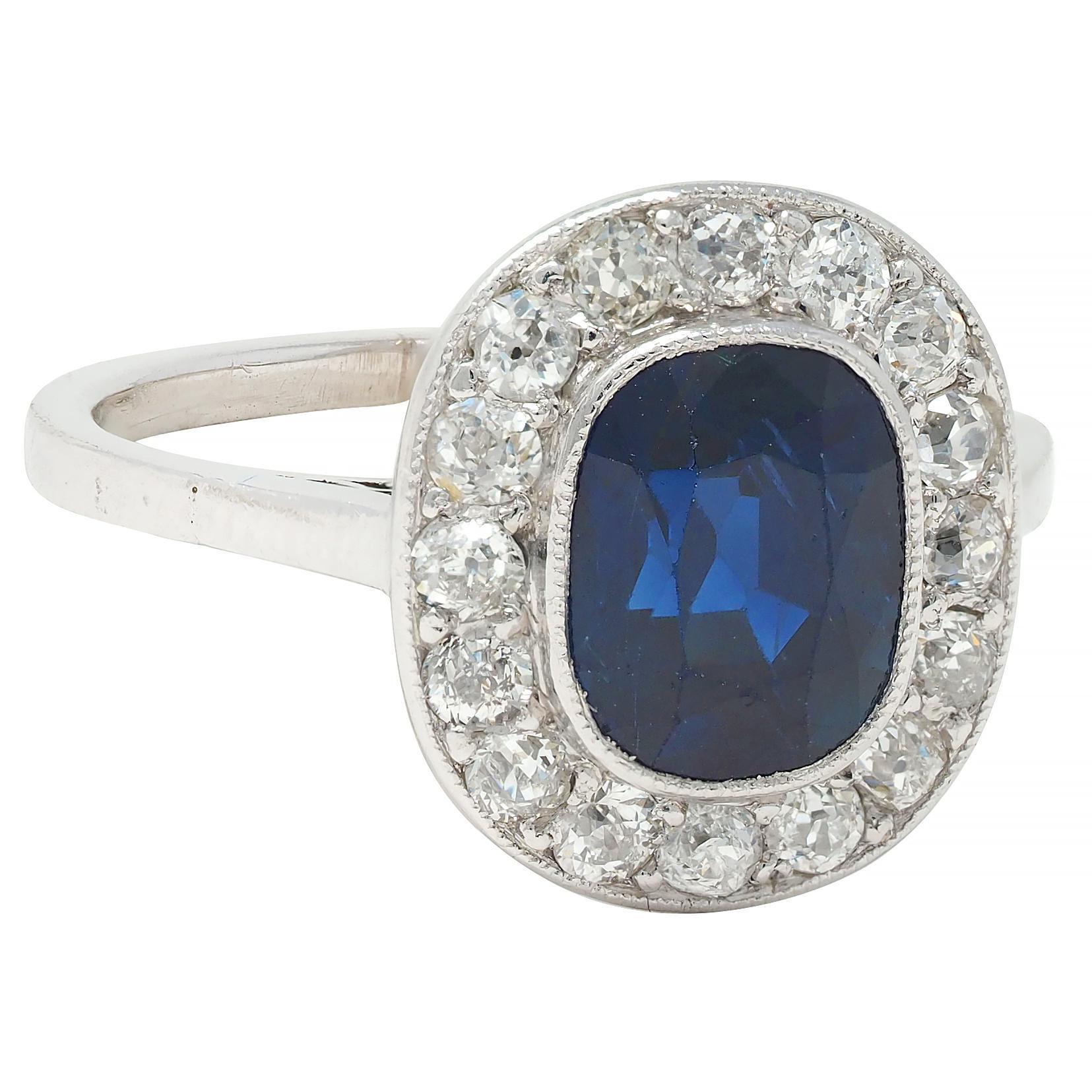 Centering a cushion cut sapphire weighing approximately 2.21 carats - transparent dark blue
Natural Cambodian in origin and displaying no indications of heat treatment
Bezel set with a recessed halo surround of old European cut diamonds
Weighing