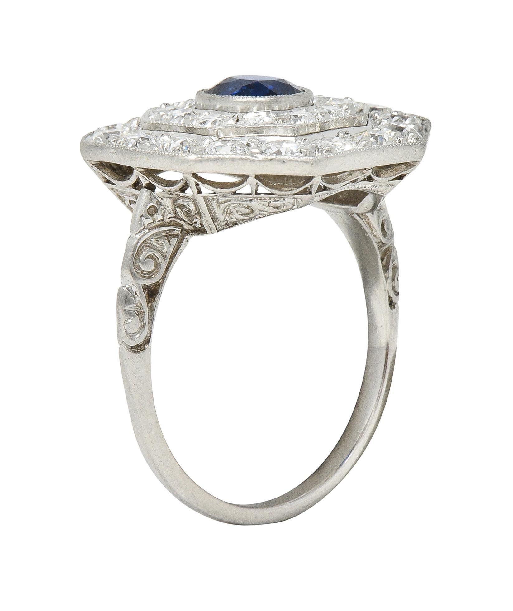 Centering a cushion cut sapphire weighing 0.82 carats - saturated deep blue in color 
Bezel set with stepped octagonal double halo surround
With old European cut diamonds weighing 2.04 carats - F/G color with VS clarity 
Accented by milgrain