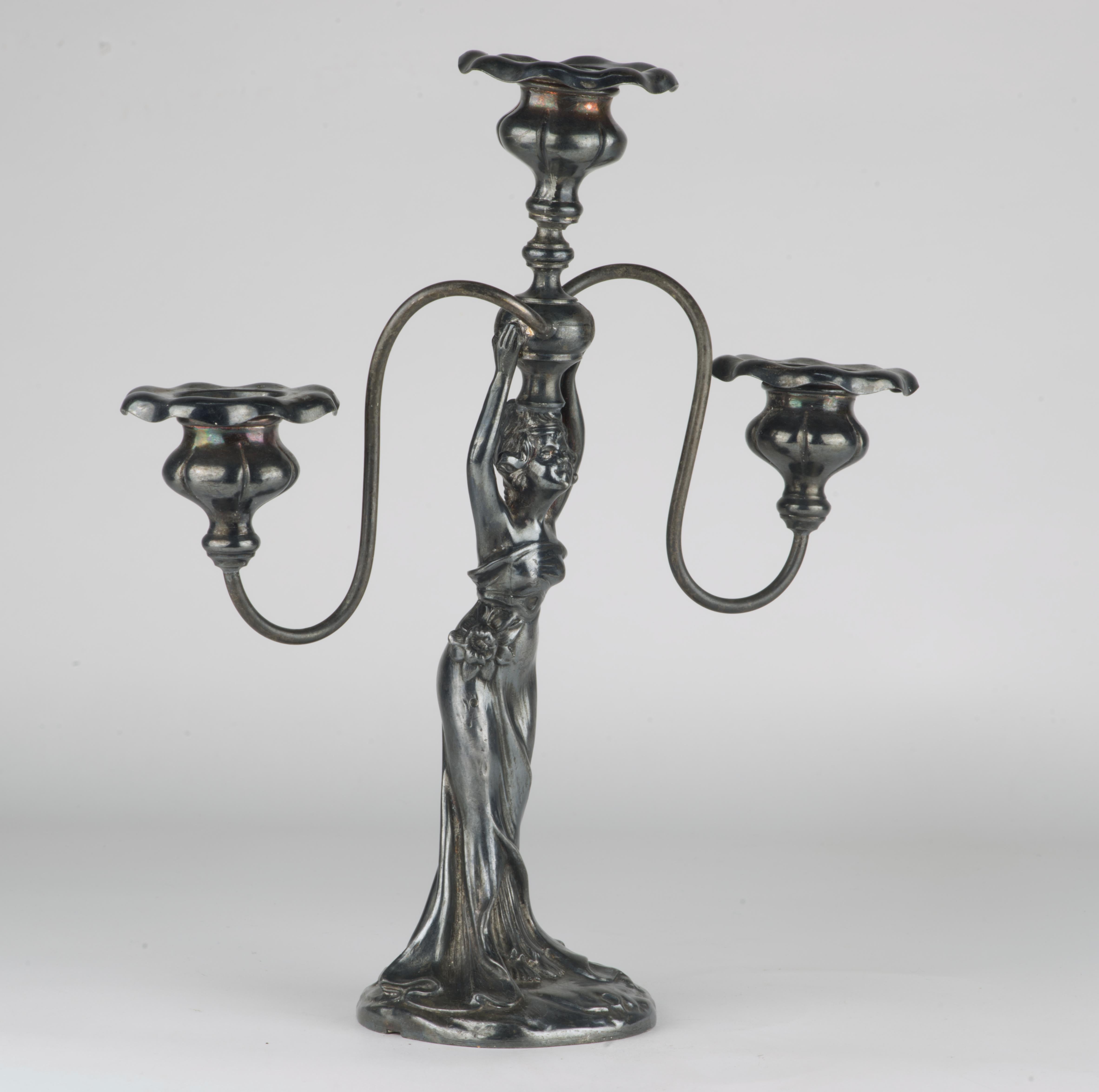  E.G. Webster and Sons silver plate candlestick has three arms with flower shaped bobeche. The stem is done in shape of a standing woman in elegant, flowing dress, standing on a rounded base and holding the central arm on a ball above her head with