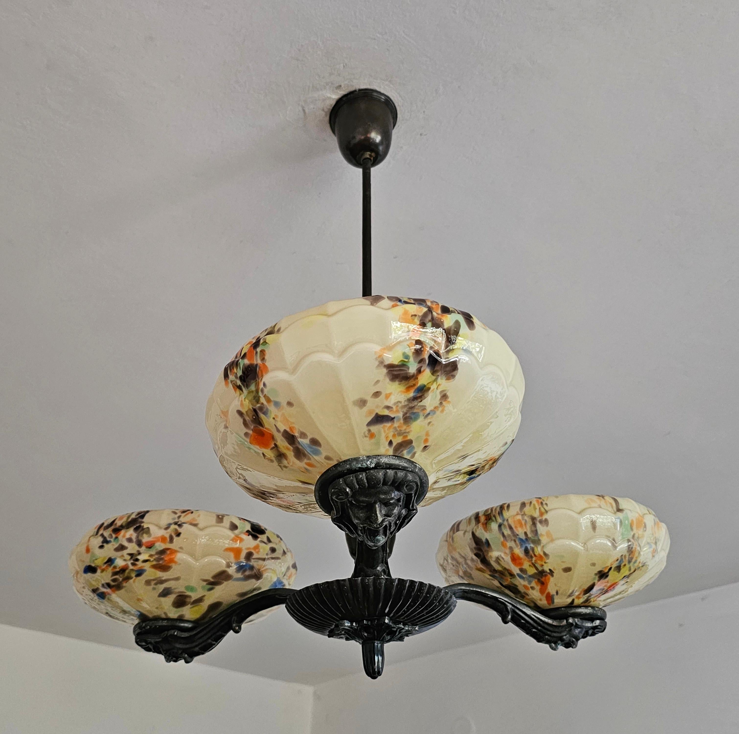 This listing features a truly spectacular chandelier, manufactured in Yugoslavia in 1930s. It belongs to Art Deco era, featuring 3 glass shades made of spotted glass in cream colour, creating a stunning composition. Each of 3 brass ends has a carved