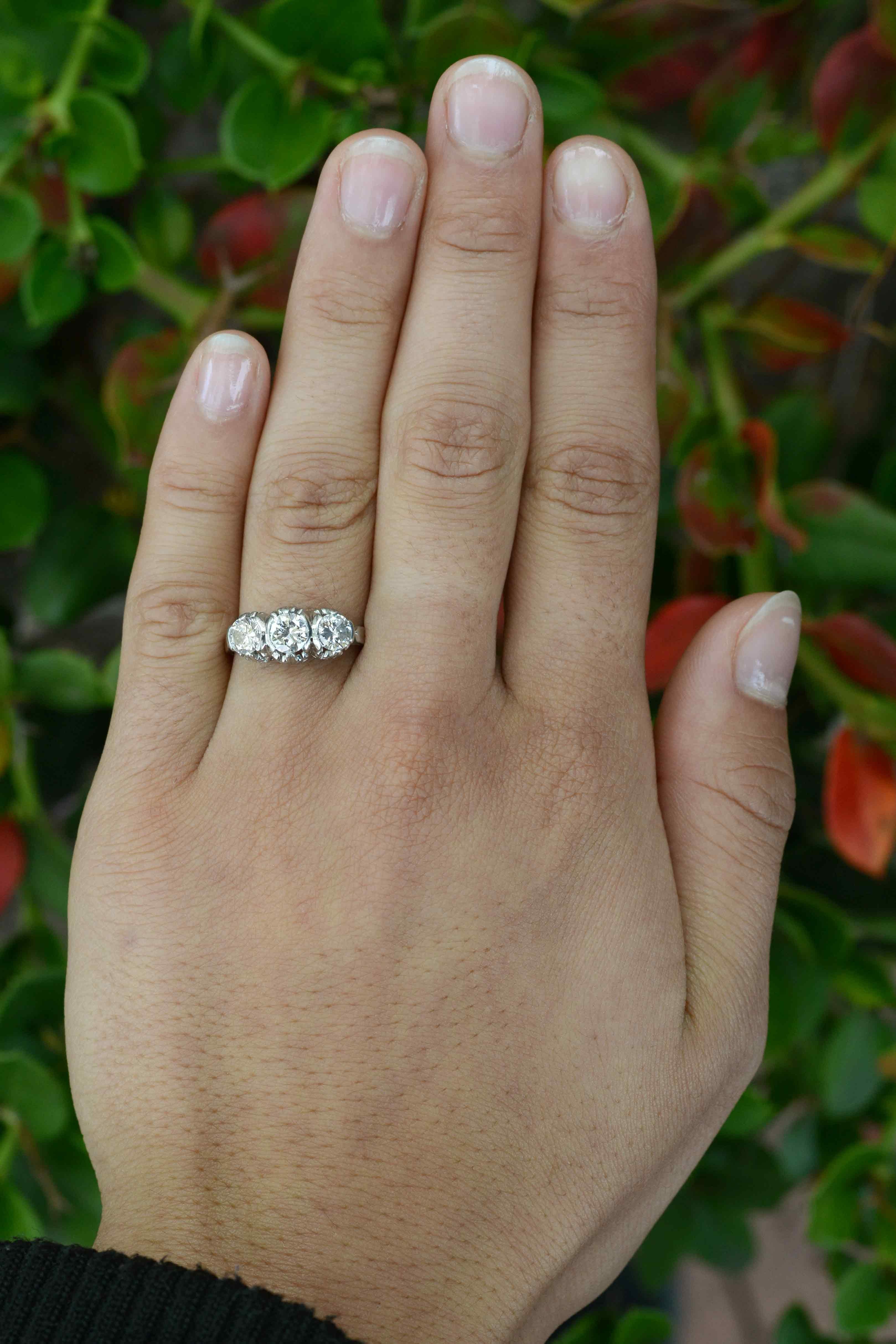 With a dainty fleur de lis crown, this fab, 3 stone Art Deco diamond engagement ring is an enduring classic. The sturdy platinum trinity or trilogy band as it is known, set with a trio of vibrant round diamonds of exceptional clarity and a
